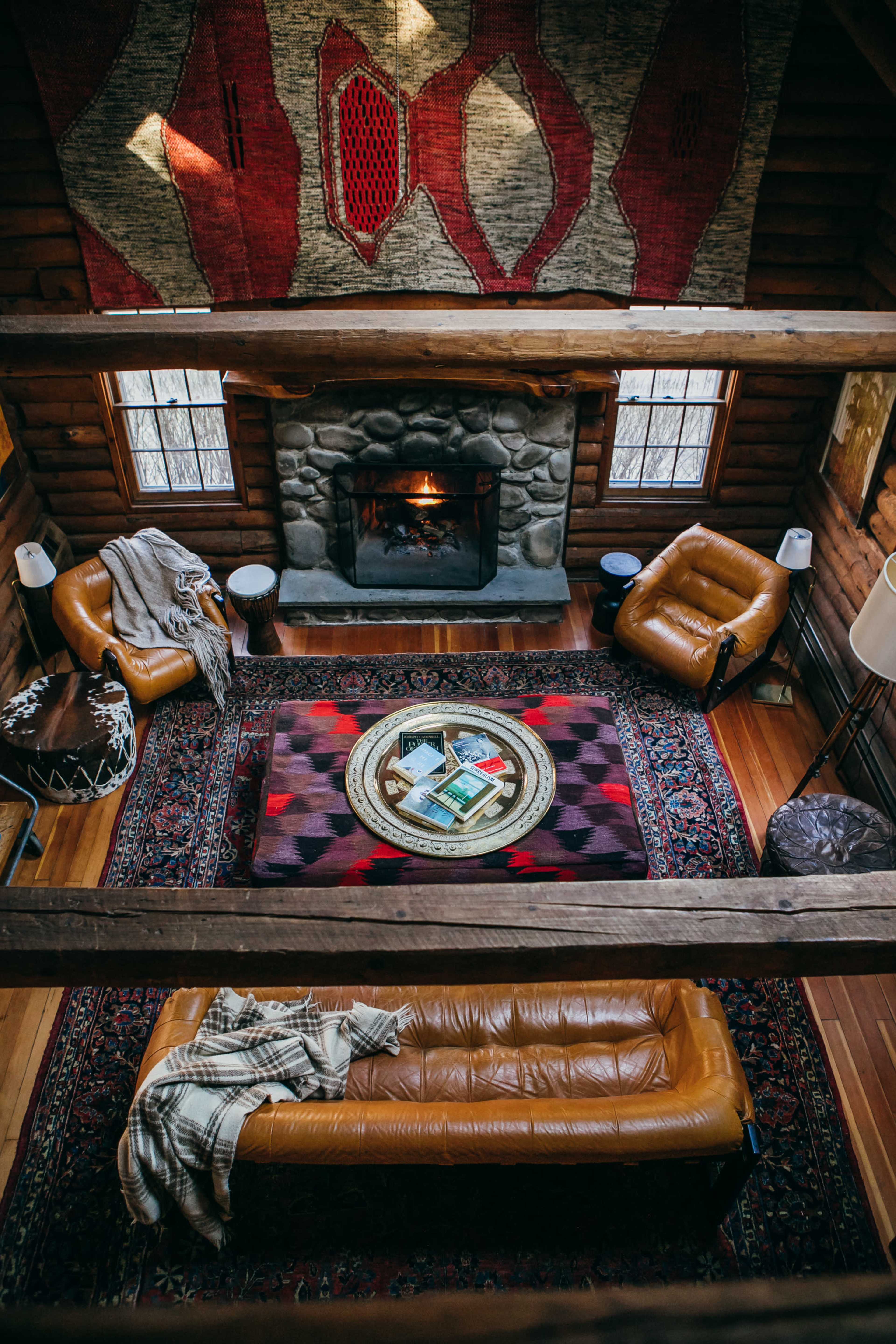 A cozy cabin interior featuring a central living area with a stone fireplace, leather furniture, and a patterned rug.