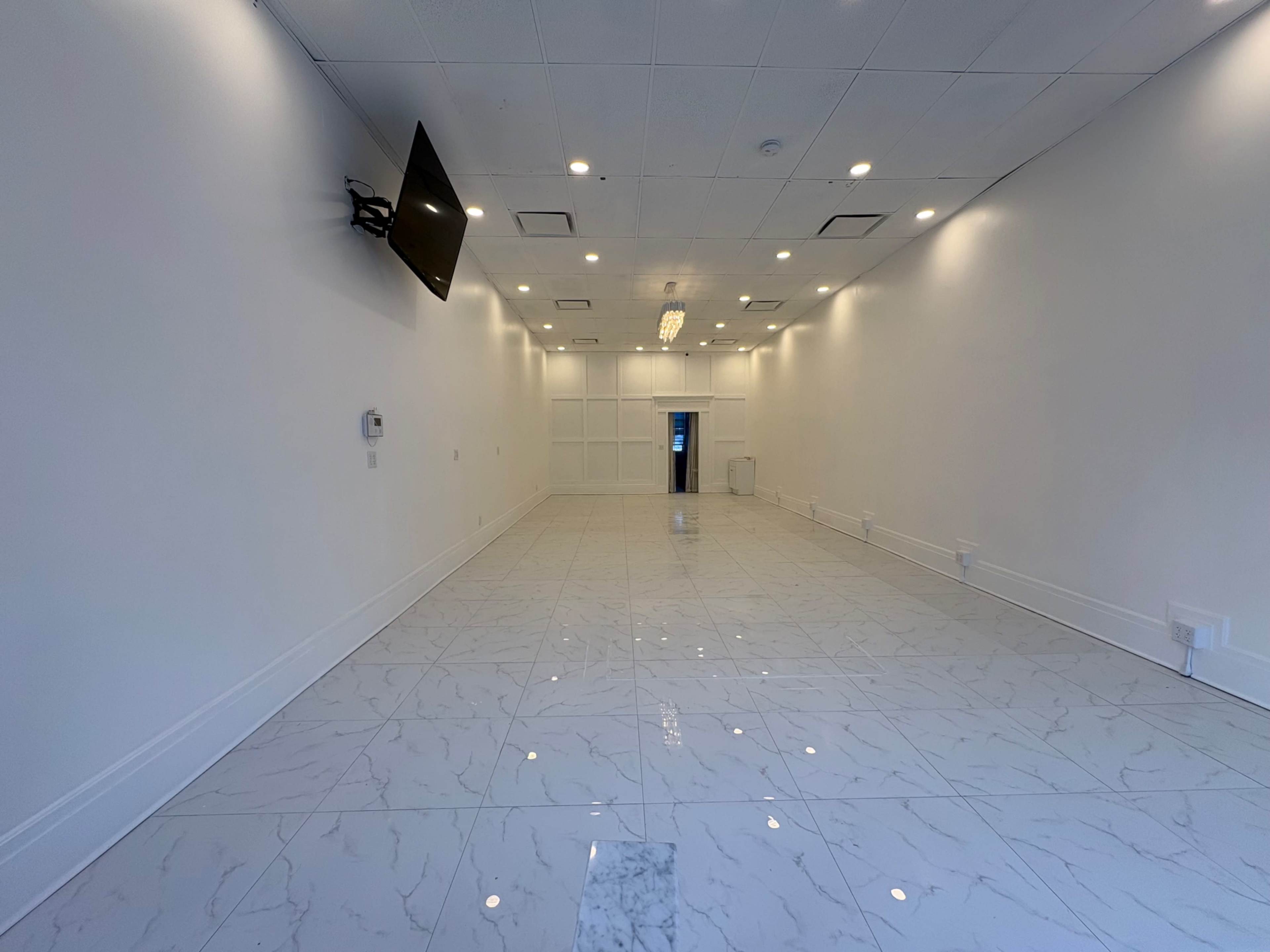 The image shows a spacious, empty room with polished marble flooring and a wall-mounted television.
