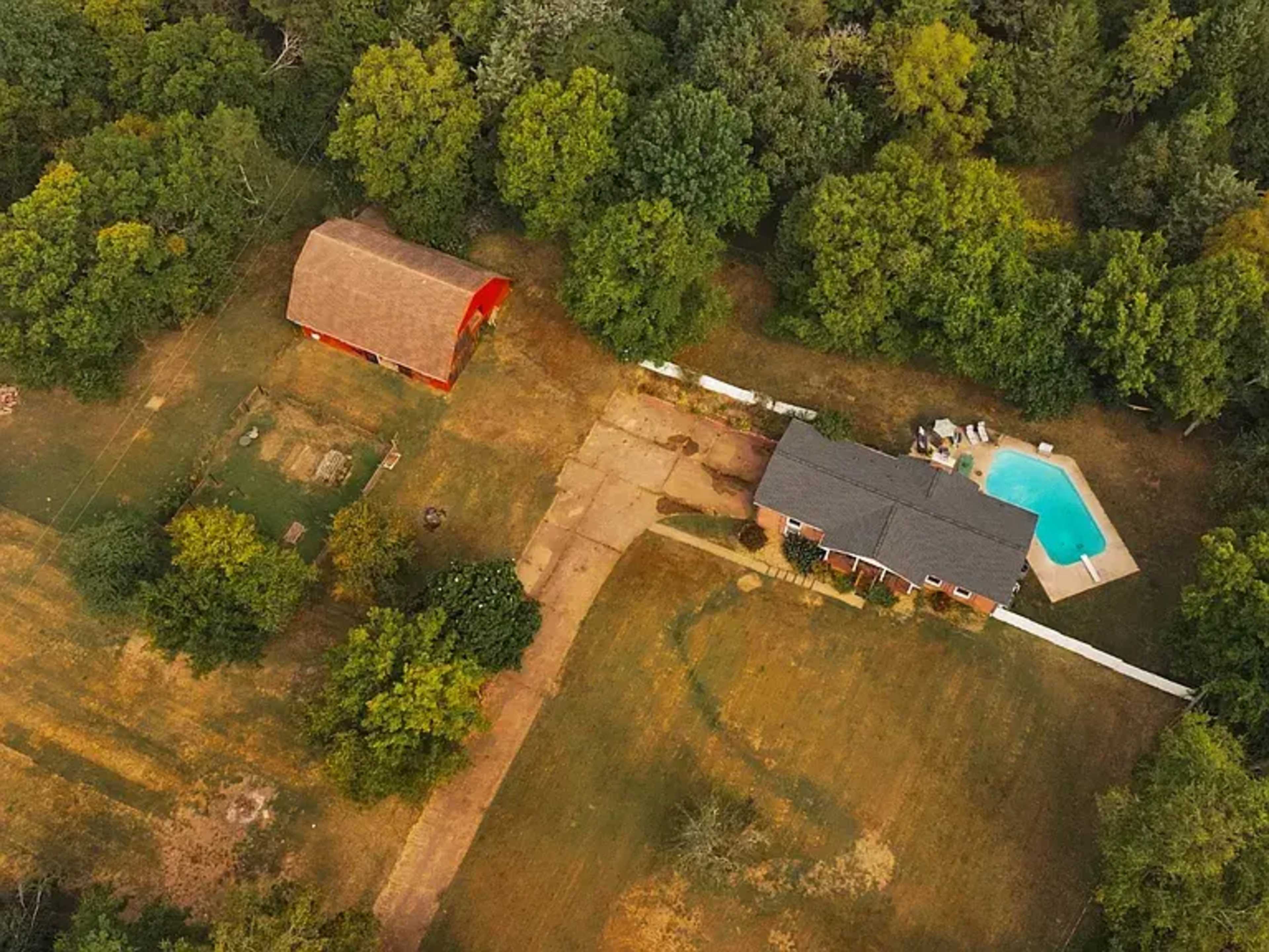 The image shows an aerial view of a house with a swimming pool adjacent to a barn, surrounded by trees and grassy areas.