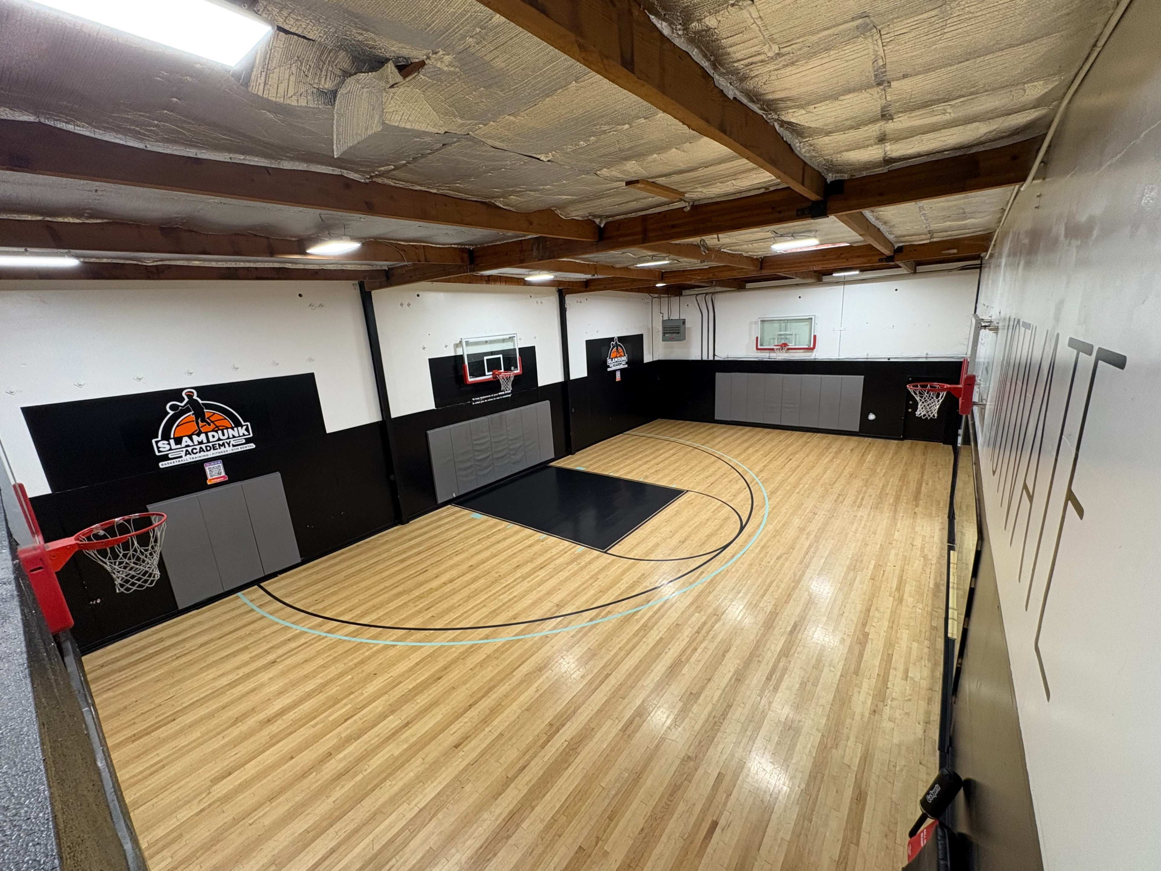 The image shows an indoor basketball court with two hoops, a painted court area, and wooden flooring.