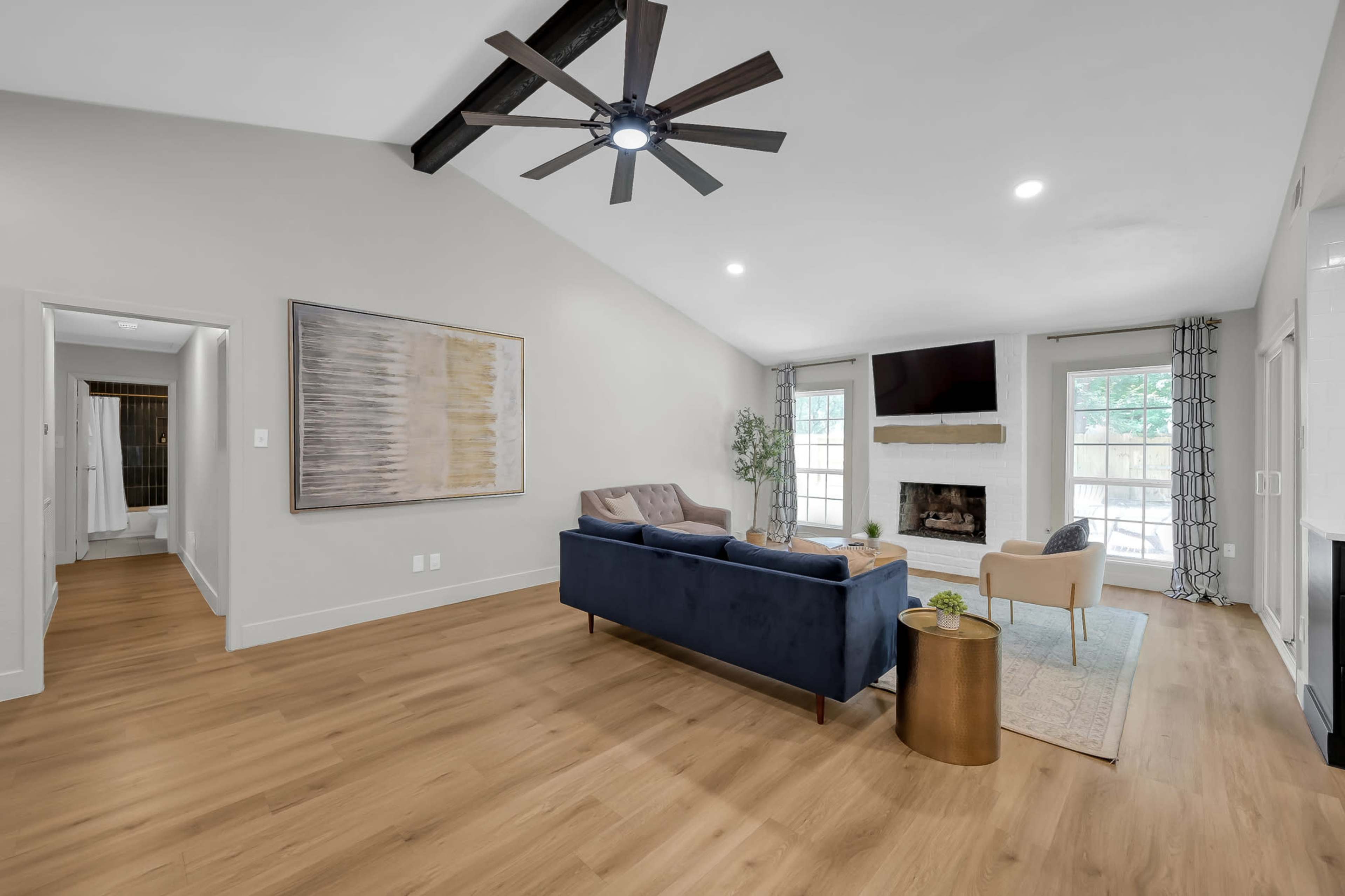 The room features a spacious living area with a blue sofa, a fireplace, and large windows allowing natural light.