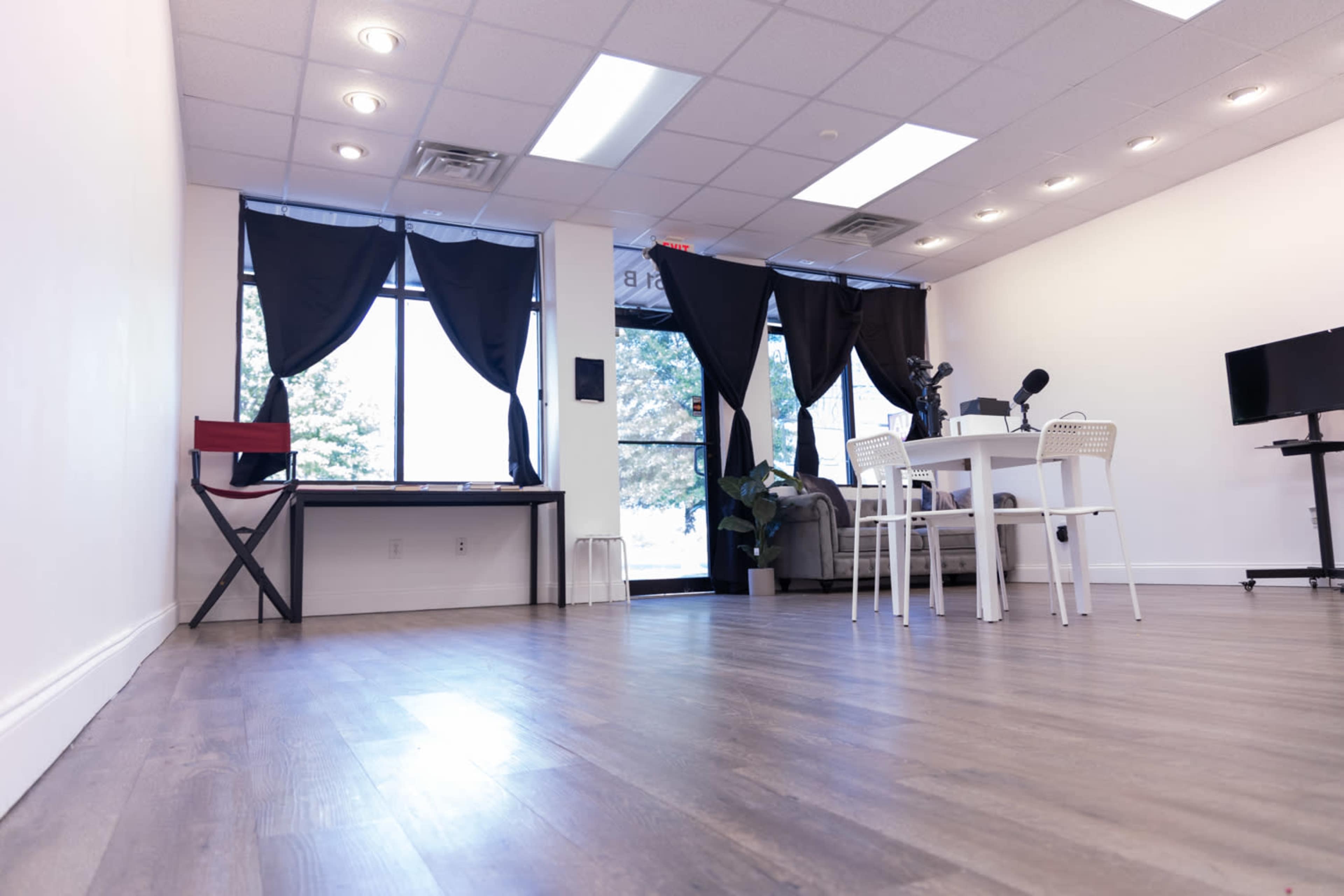 A bright, spacious room with a table and chairs, a desk, and large windows covered by black curtains.
