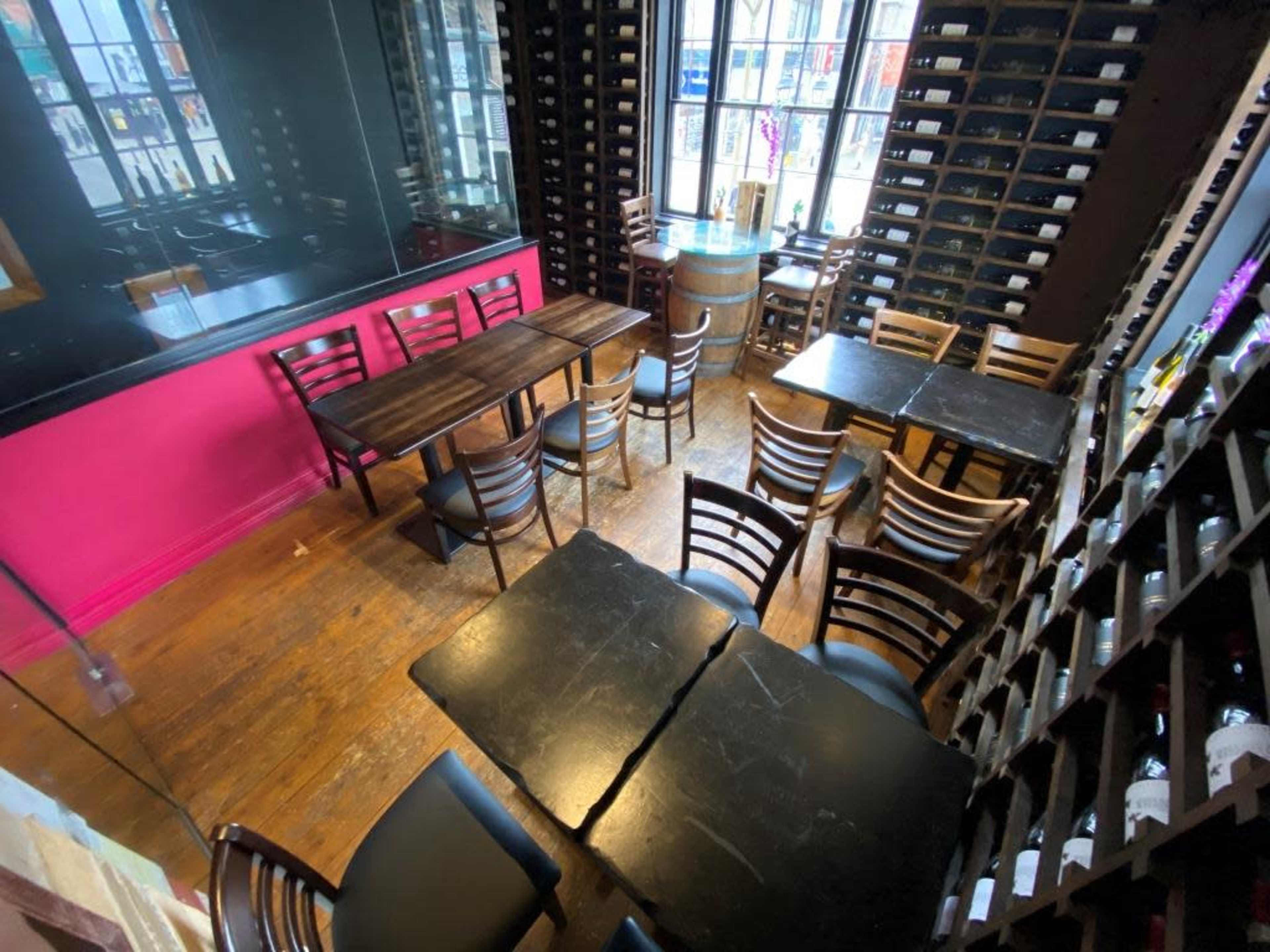 A restaurant interior featuring several wooden tables and chairs arranged against walls lined with wine bottles.