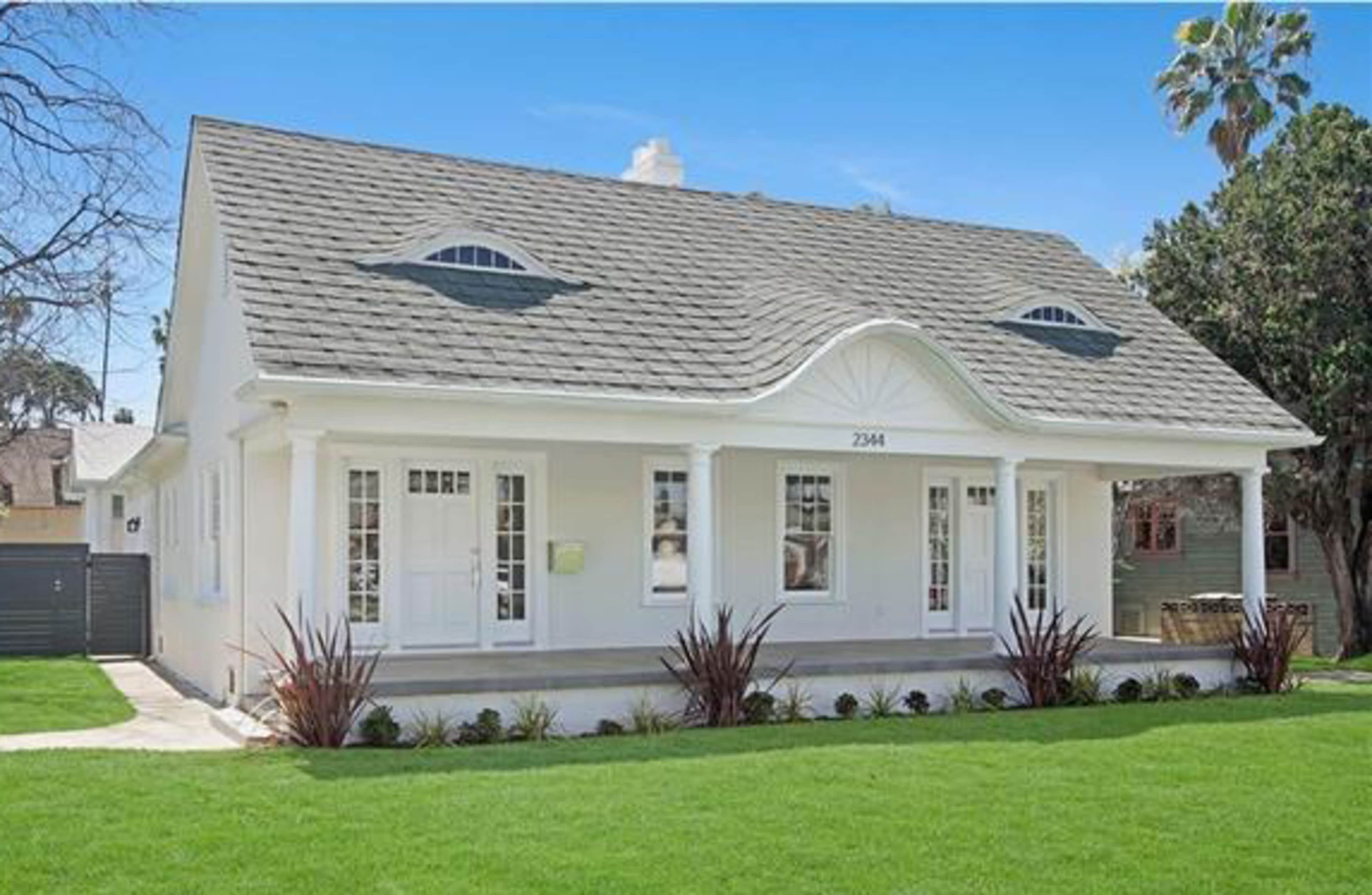 A single-story white house with a distinctive curved roof, large front windows, and a well-manicured lawn.