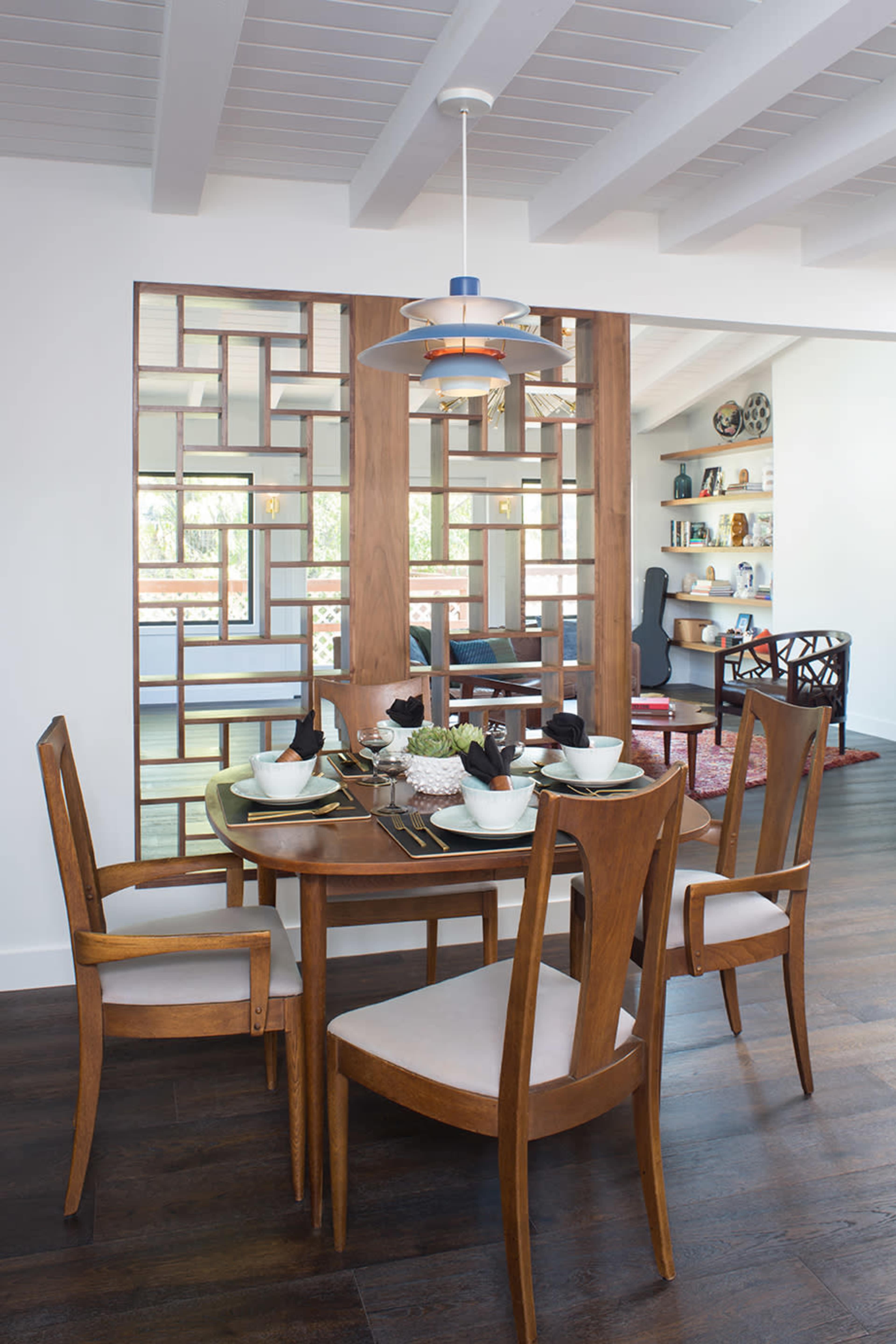 A round wooden dining table is set with tableware, surrounded by four chairs, while a modern decorative partition divides the dining area from a living space in the background.