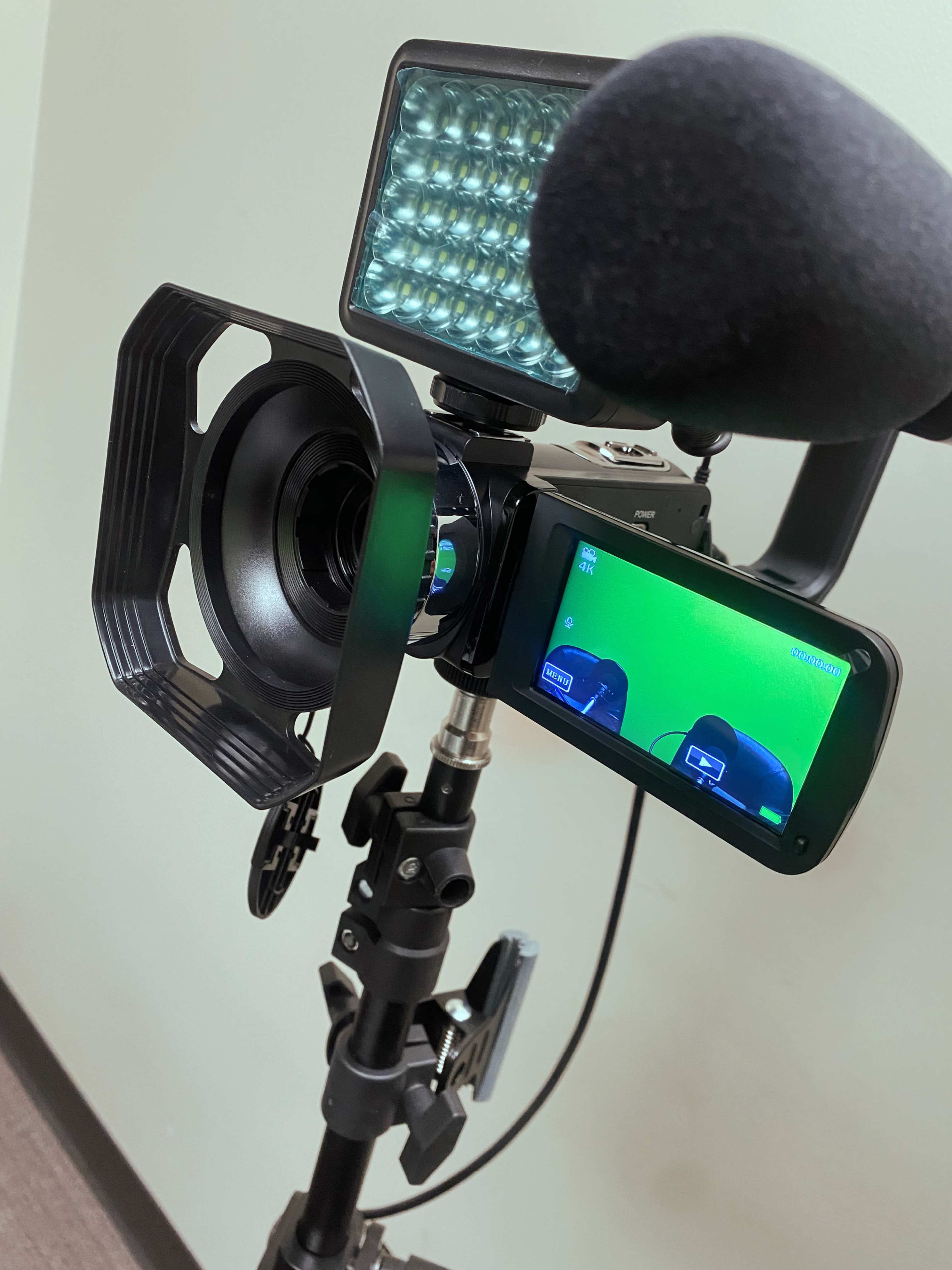 A camera setup with a microphone, a light panel, and a viewfinder is mounted on a tripod.