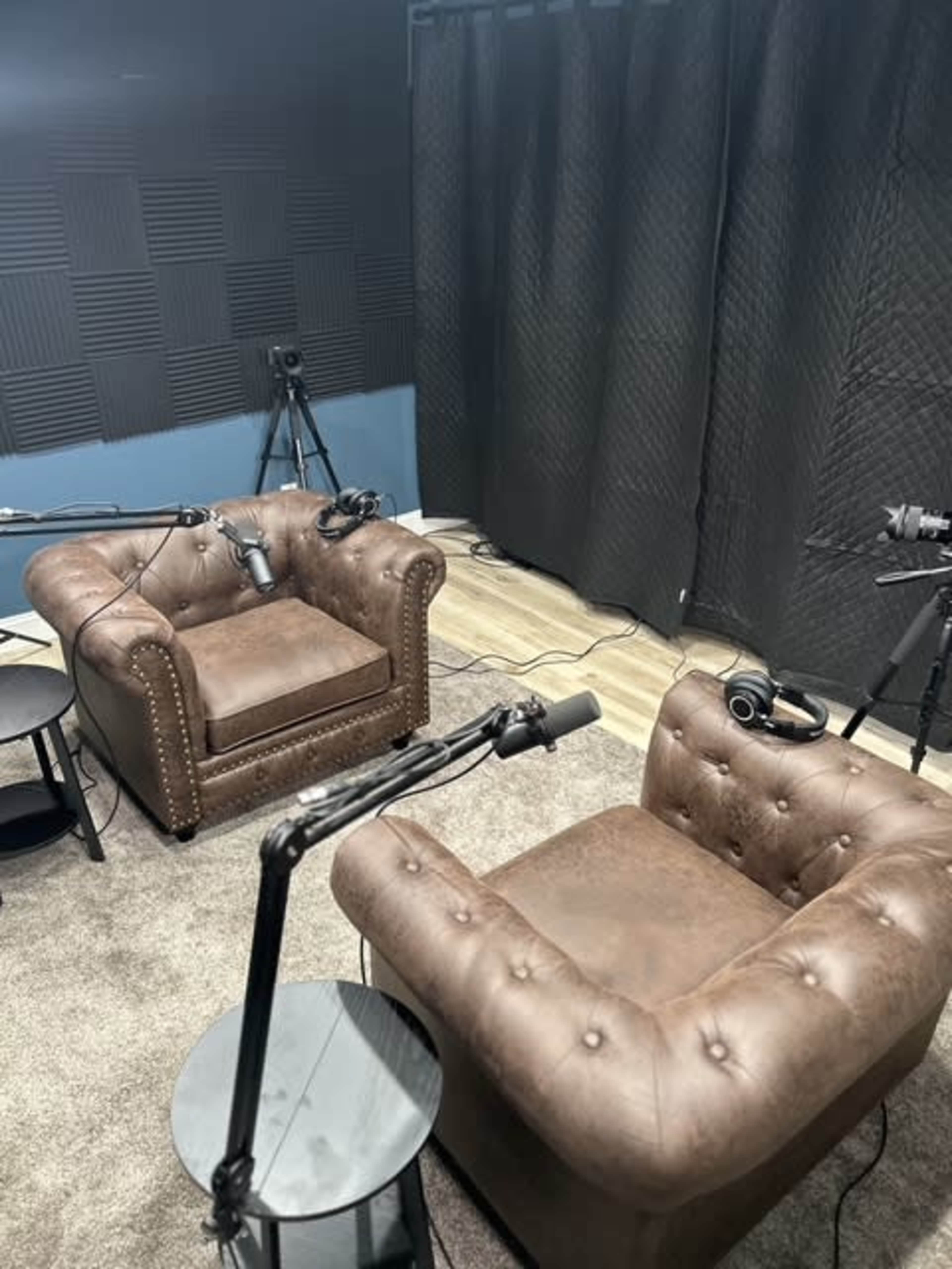 The image shows a recording studio with two brown leather chairs and microphones positioned for a conversation.