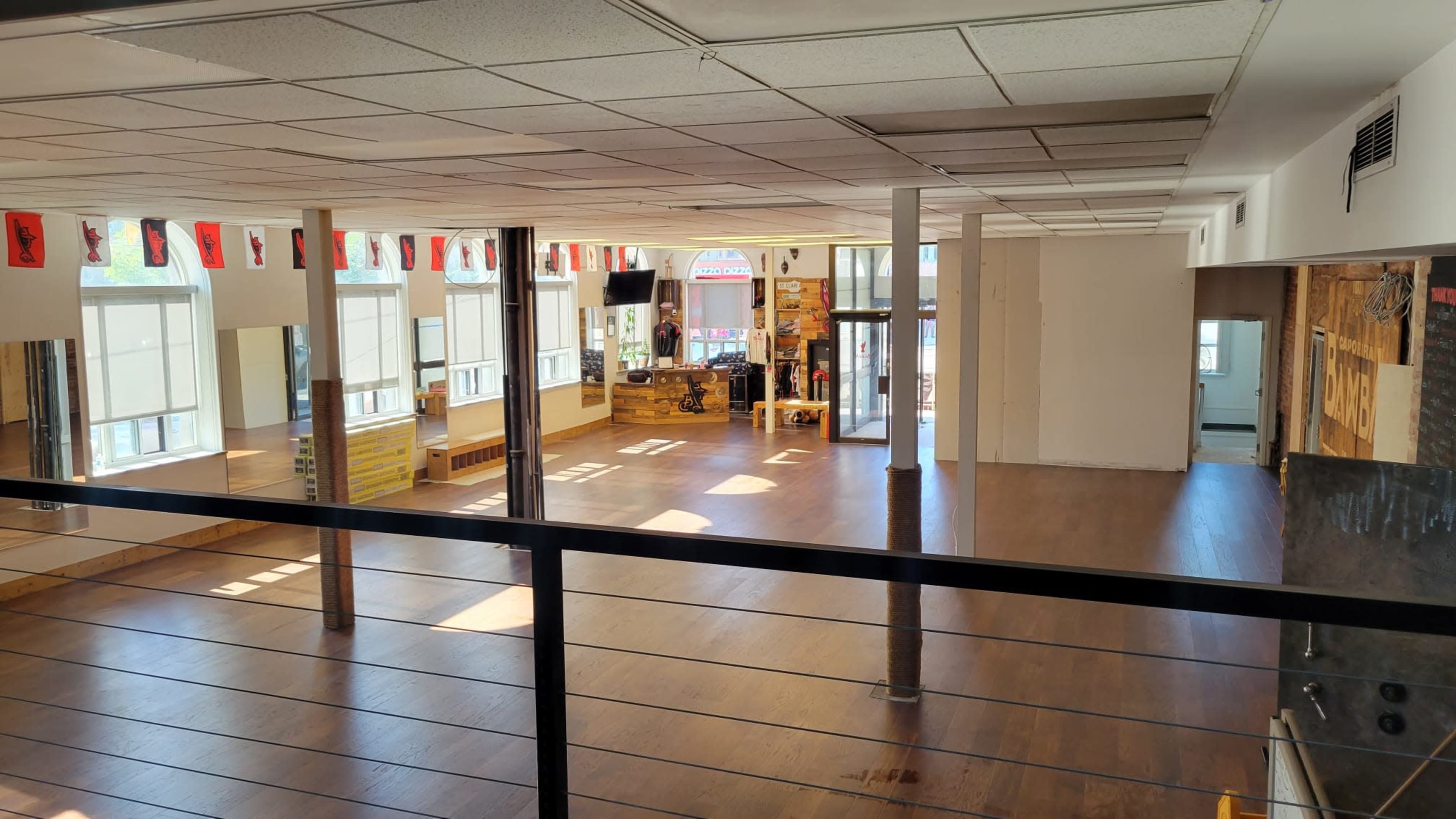 A spacious, empty studio with wooden flooring, large windows, and mirrors on the walls.