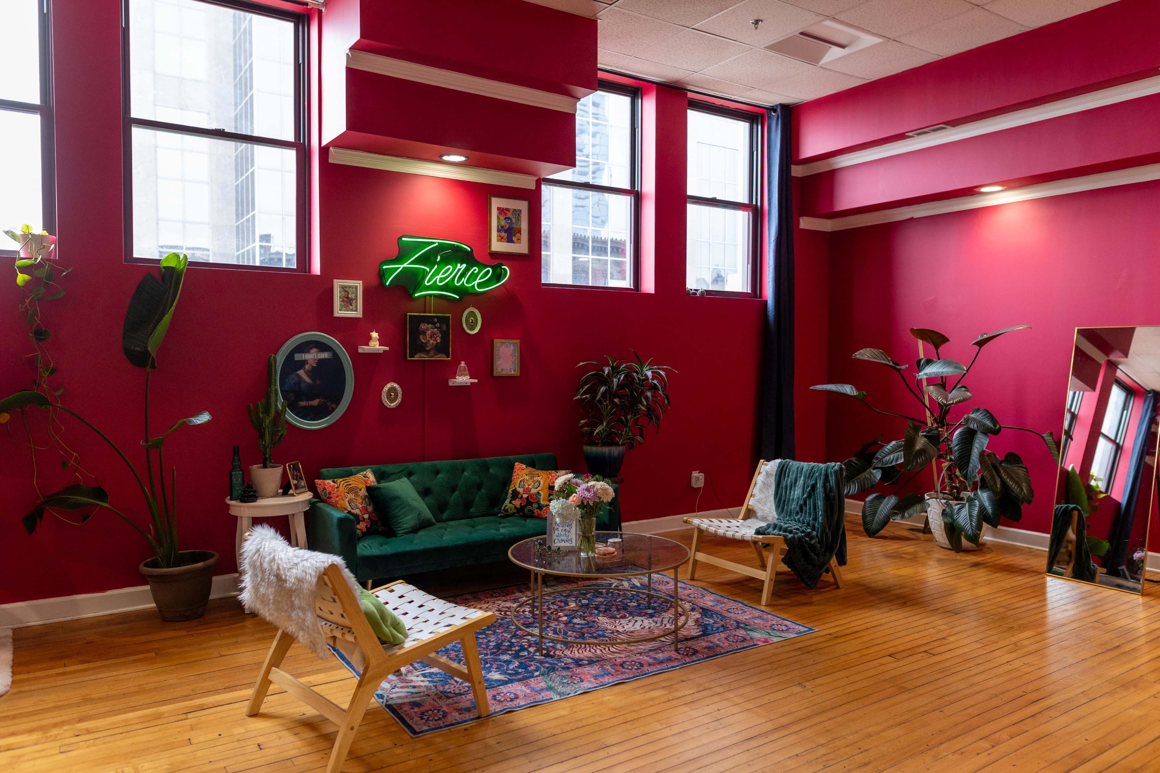 The image shows a vibrant indoor space with pink walls, a green velvet sofa, decorative plants, and a colorful area rug.