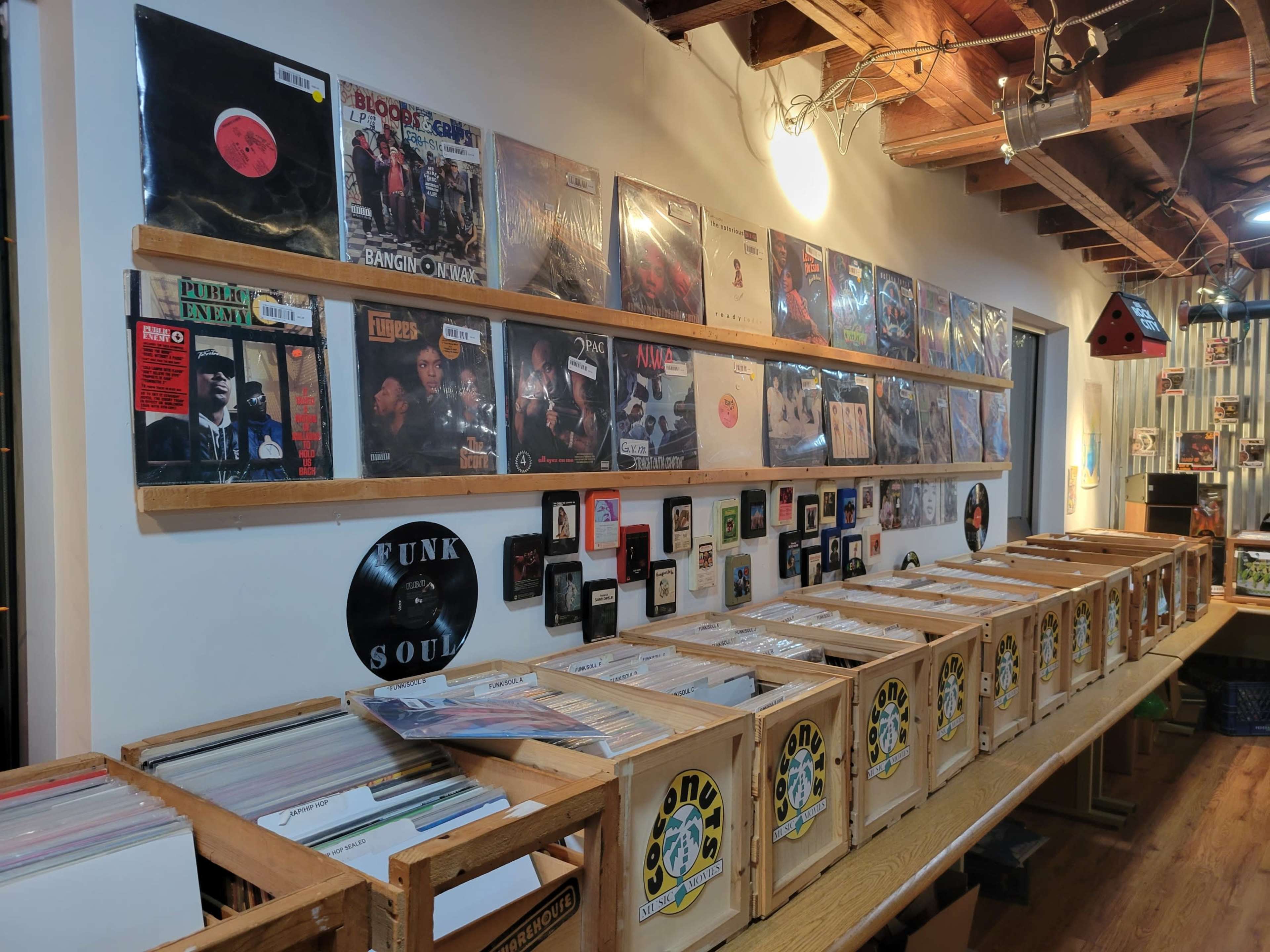 A wall of vinyl records is displayed above wooden crates filled with albums in a record store.