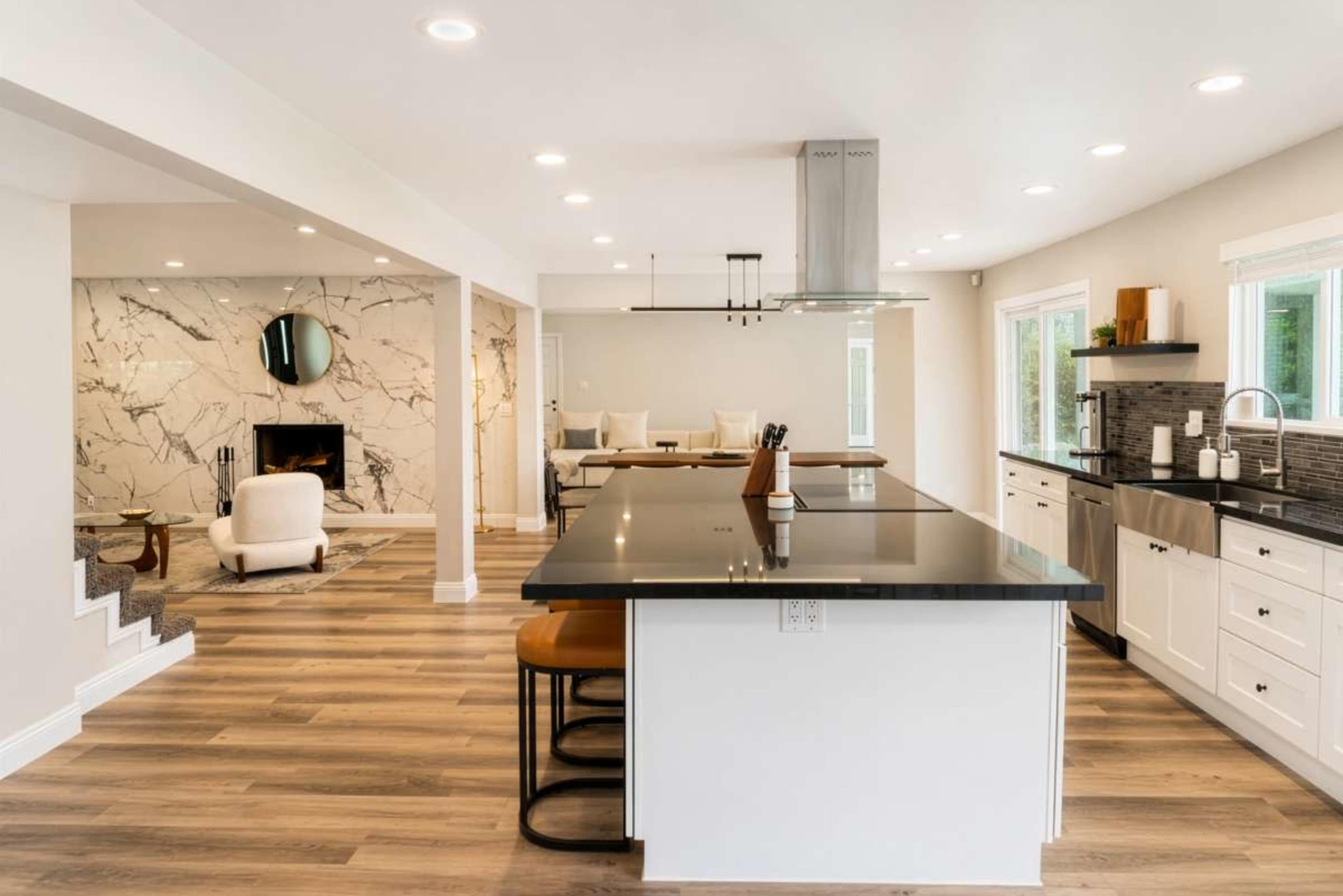 The image shows a modern kitchen with a black countertop, white cabinets, and an adjacent living area featuring a fireplace and seating.