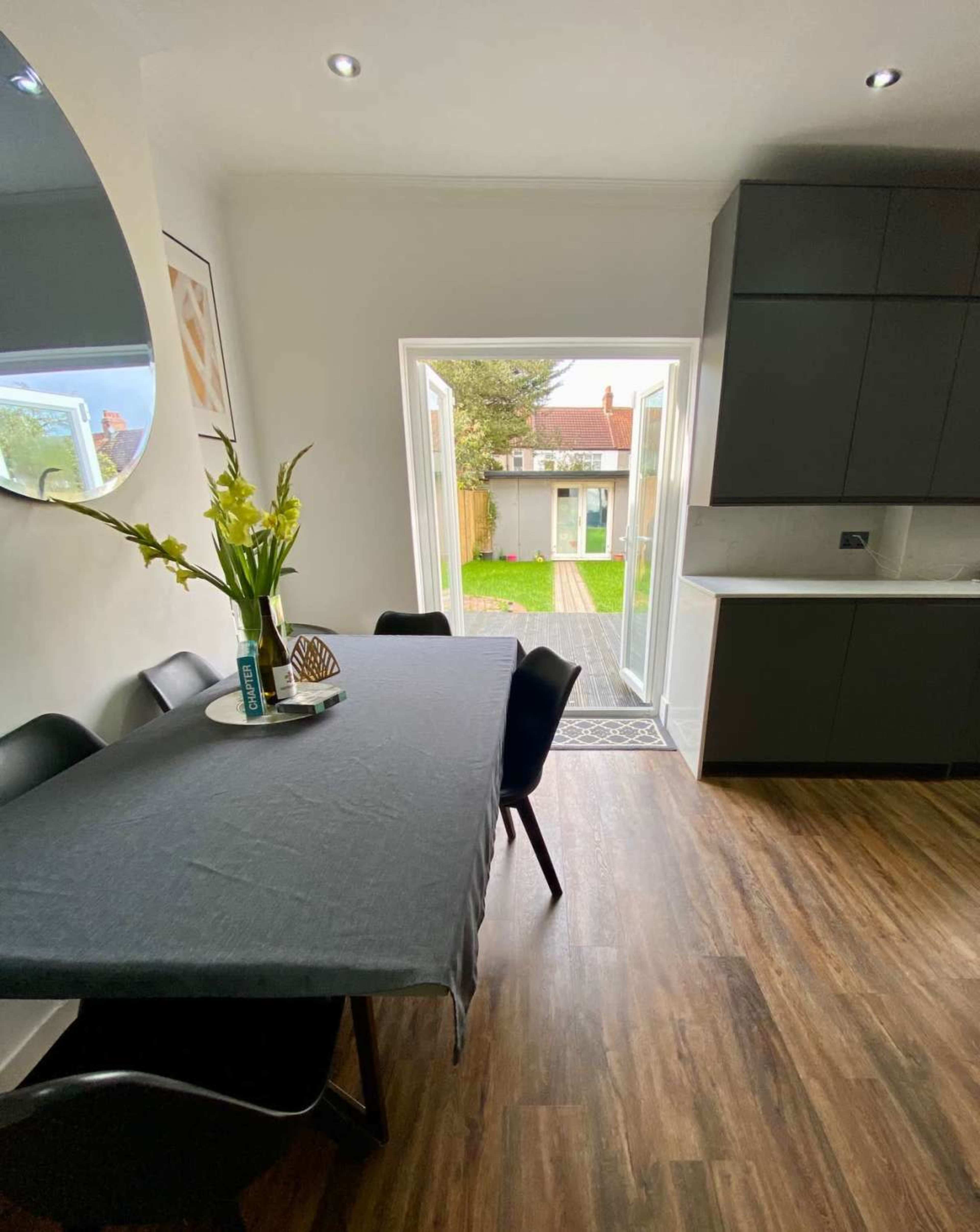 A dining area features a dark table with chairs, a vase of flowers, and an open door leading to a grassy backyard.