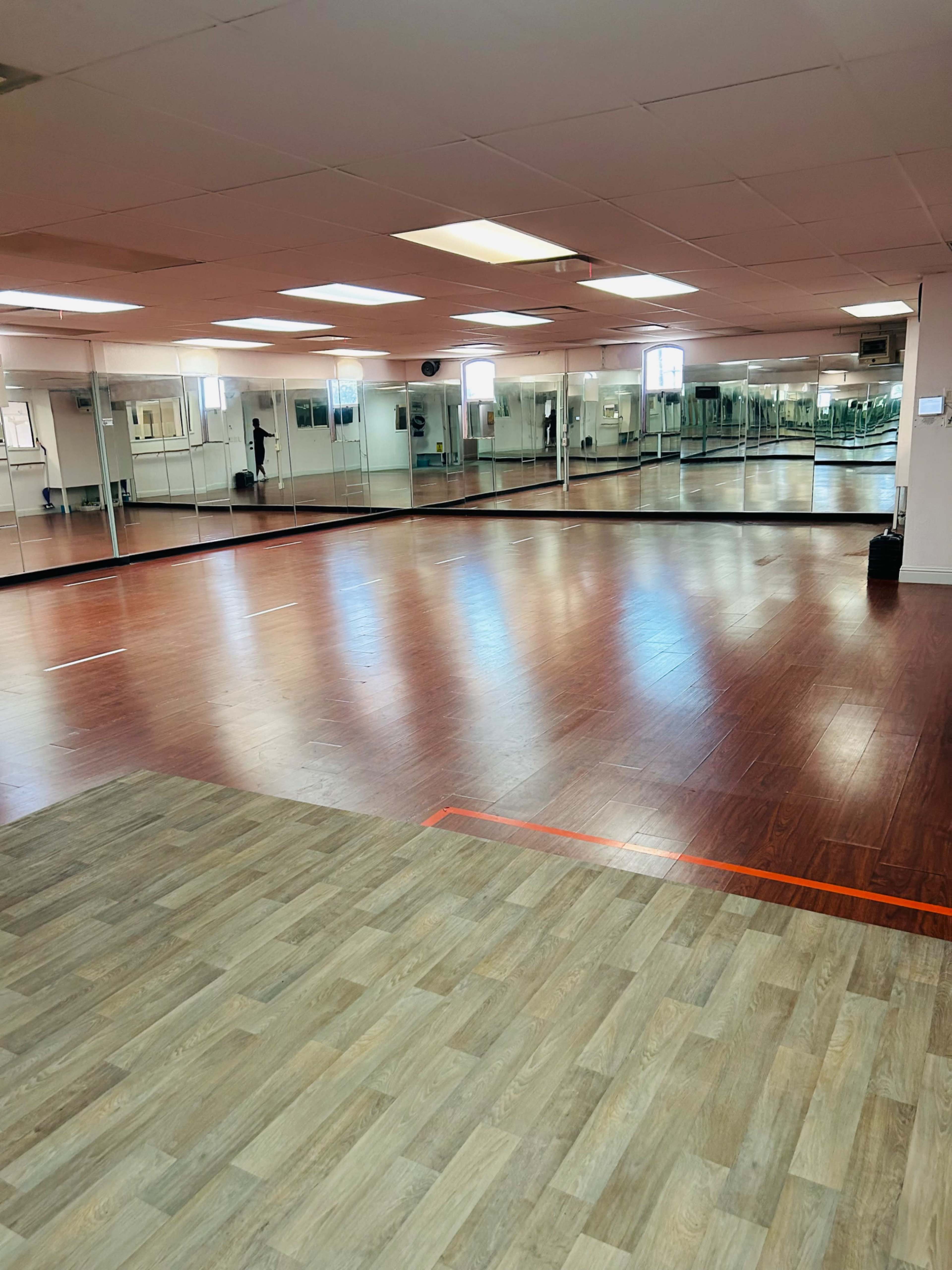 A spacious dance studio with mirrored walls, polished wooden floors, and large windows allowing natural light.