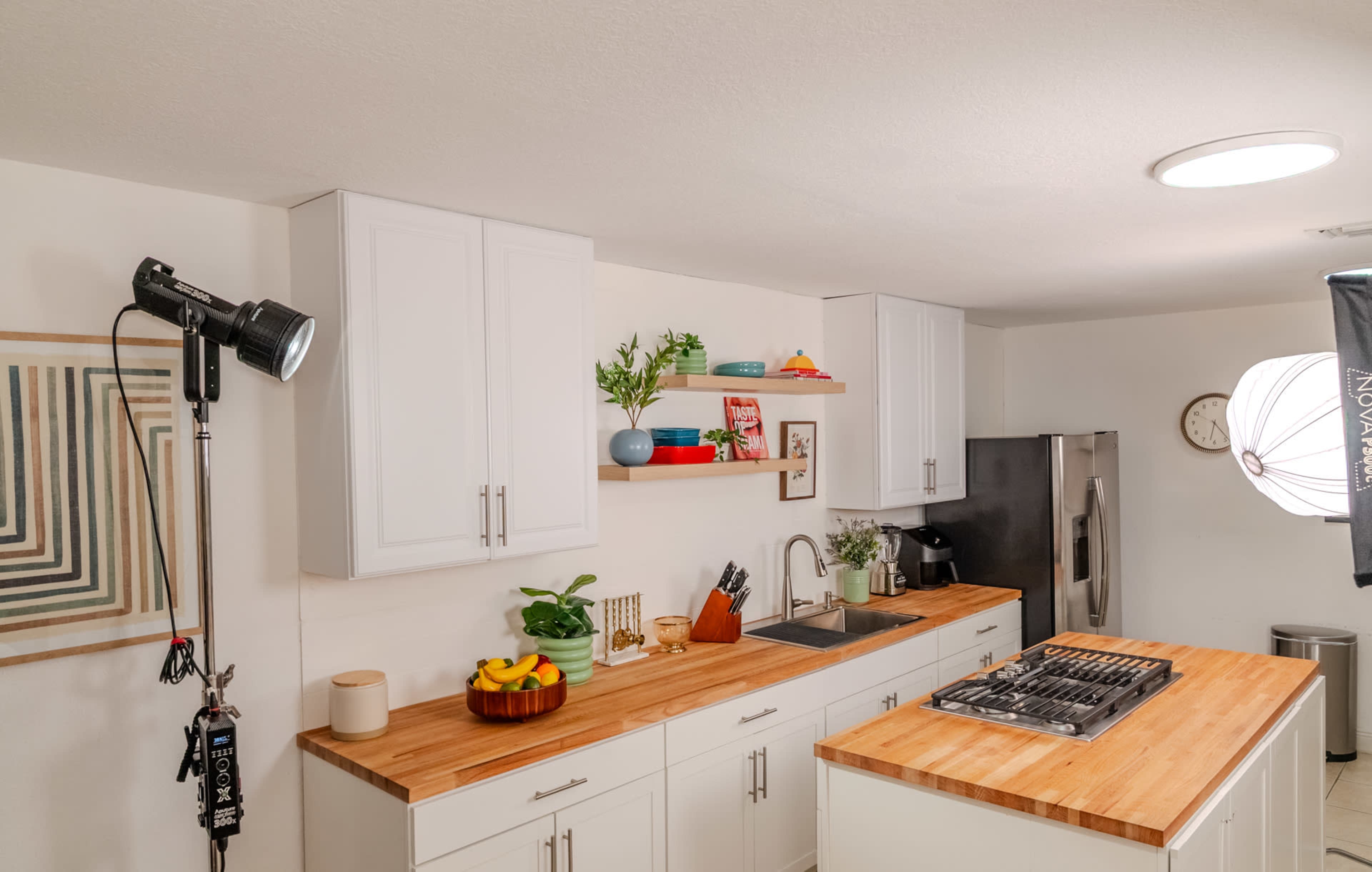 A modern kitchen features white cabinets, a wooden countertop, and an island with a gas stove, along with decorative plants and kitchenware.