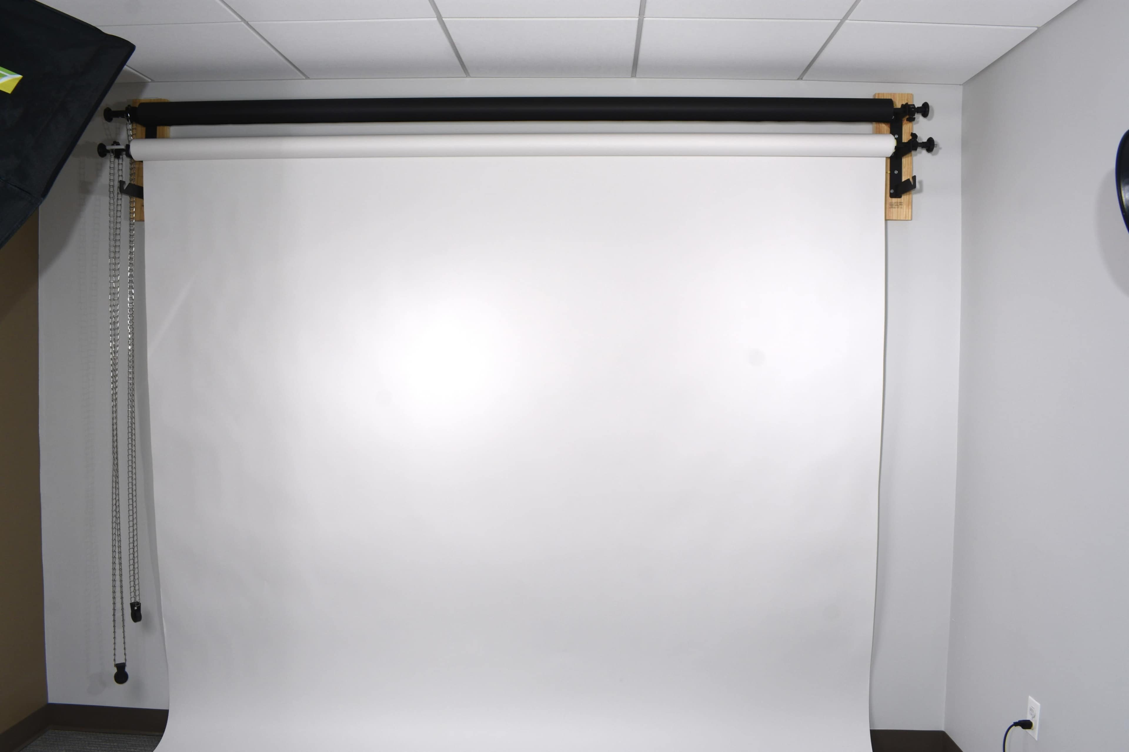 A photography studio setup with a white backdrop mounted on a support system against a plain wall.