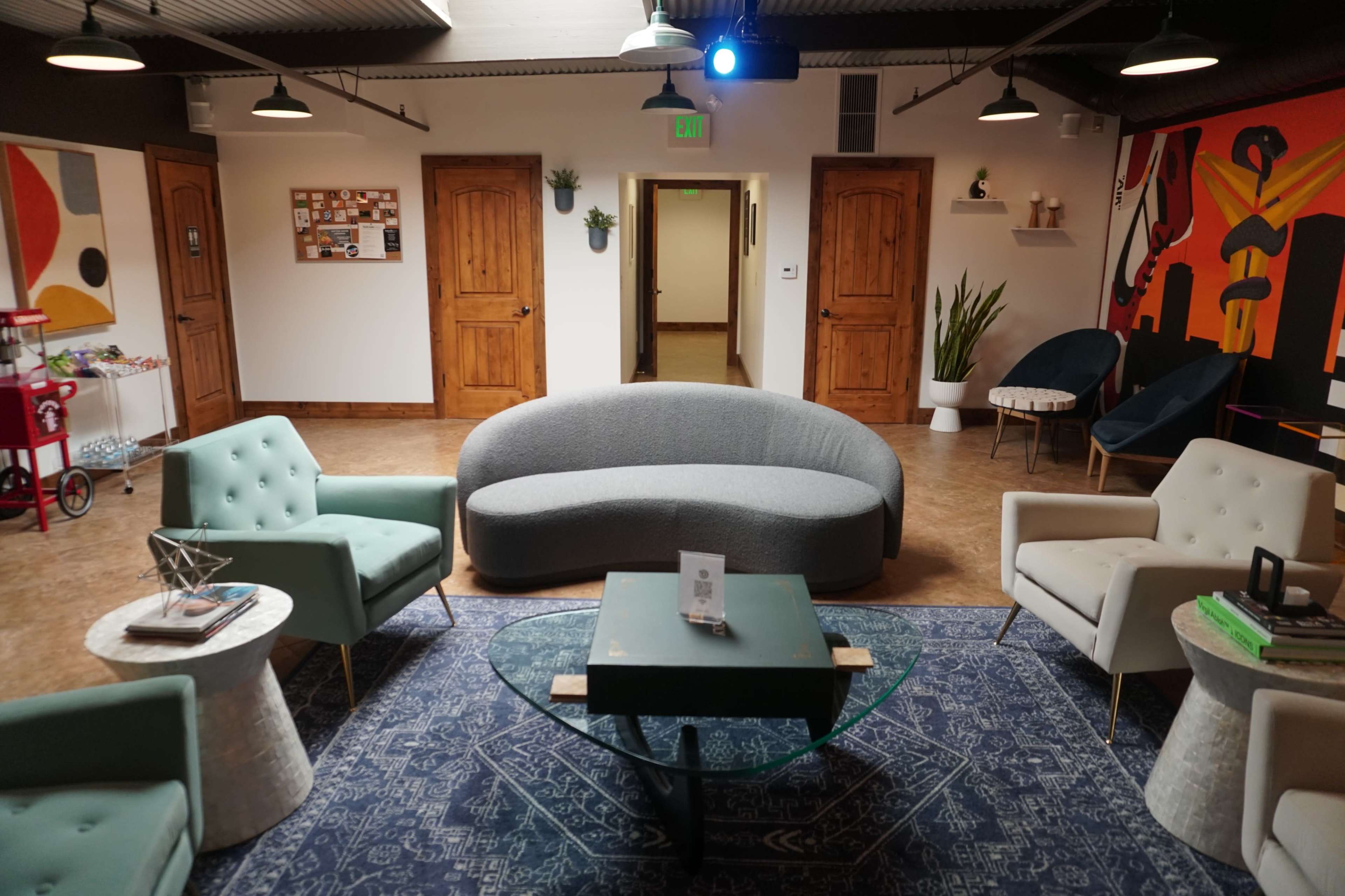 A modern, open lounge area featuring a curved gray sofa, a green coffee table, and various seating options against a backdrop of wooden doors and artistic walls.