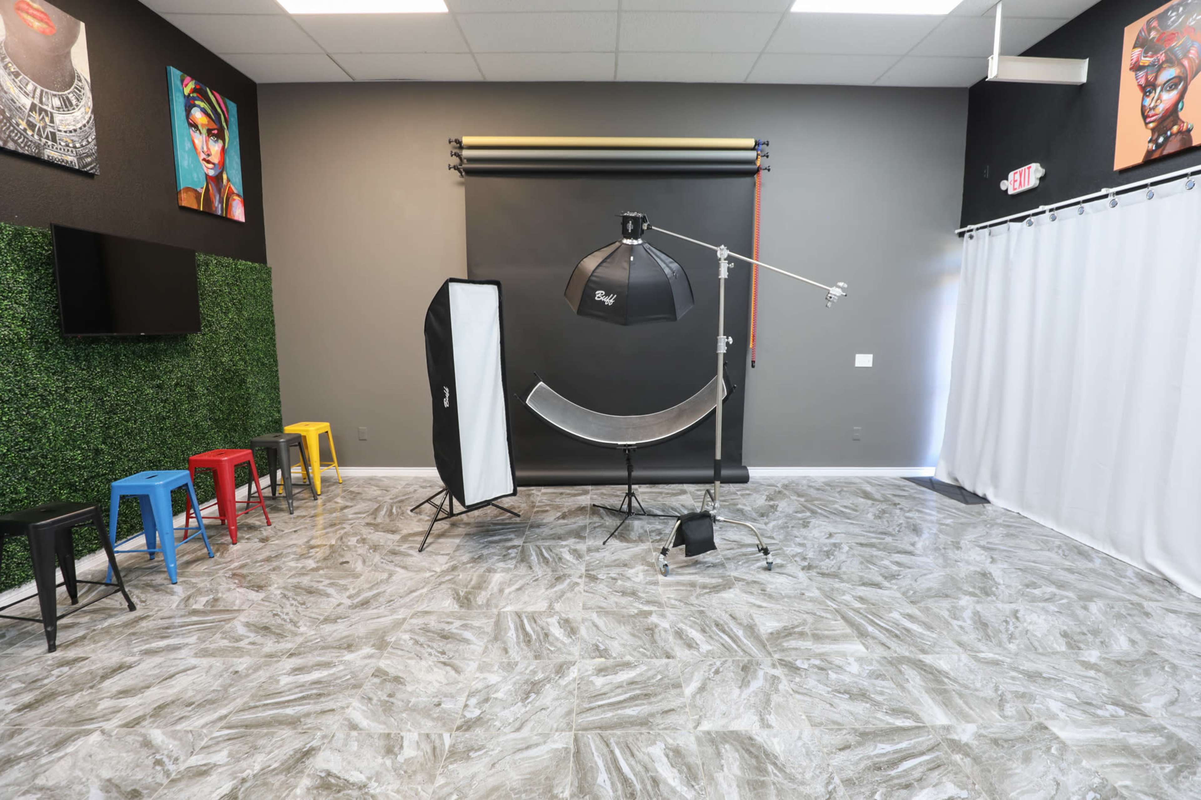 A photography studio equipped with a backdrop, lighting equipment, and colorful stools arranged against a green wall.