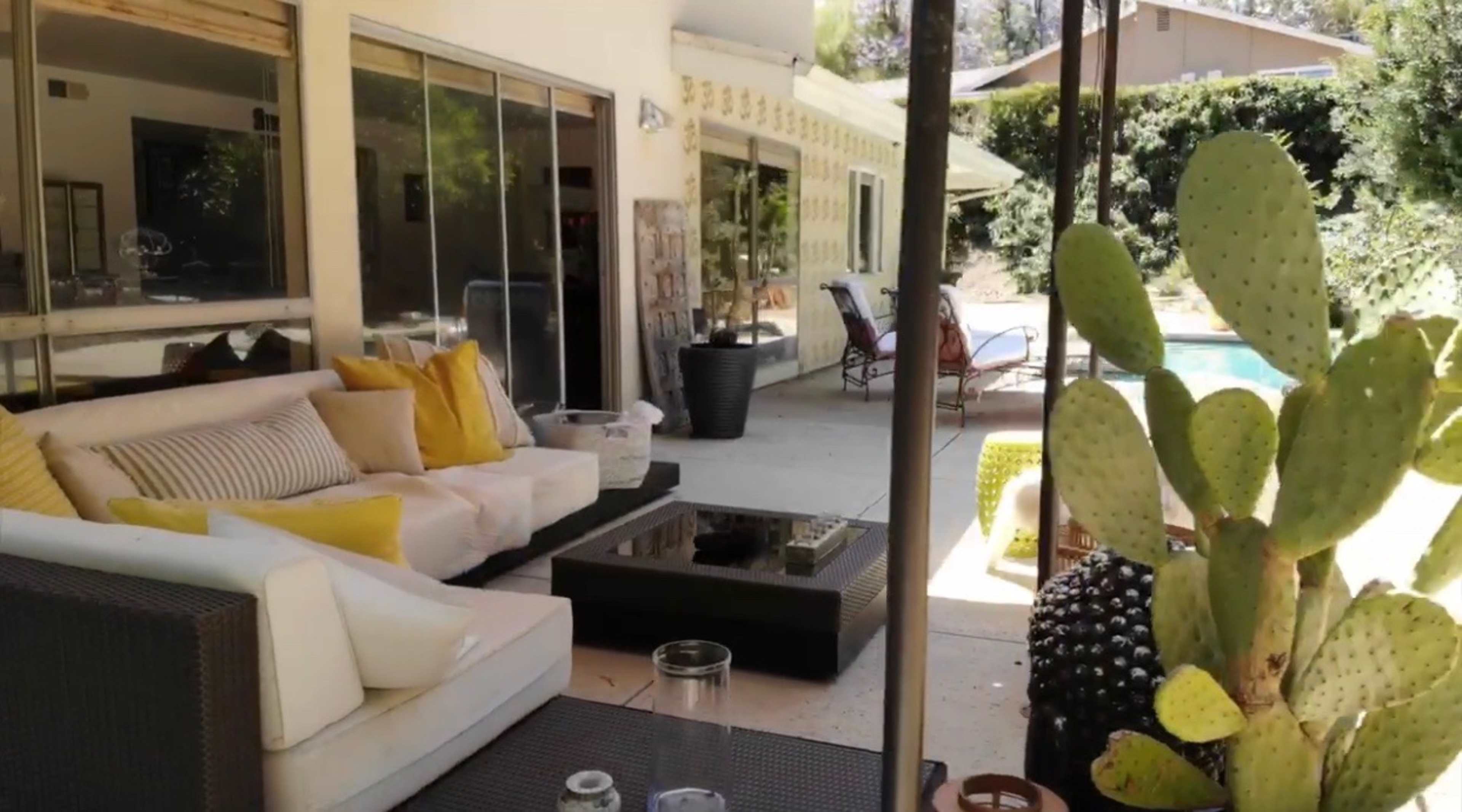 A patio area features a modern seating arrangement, coffee table, and a cactus plant, all adjacent to a swimming pool.