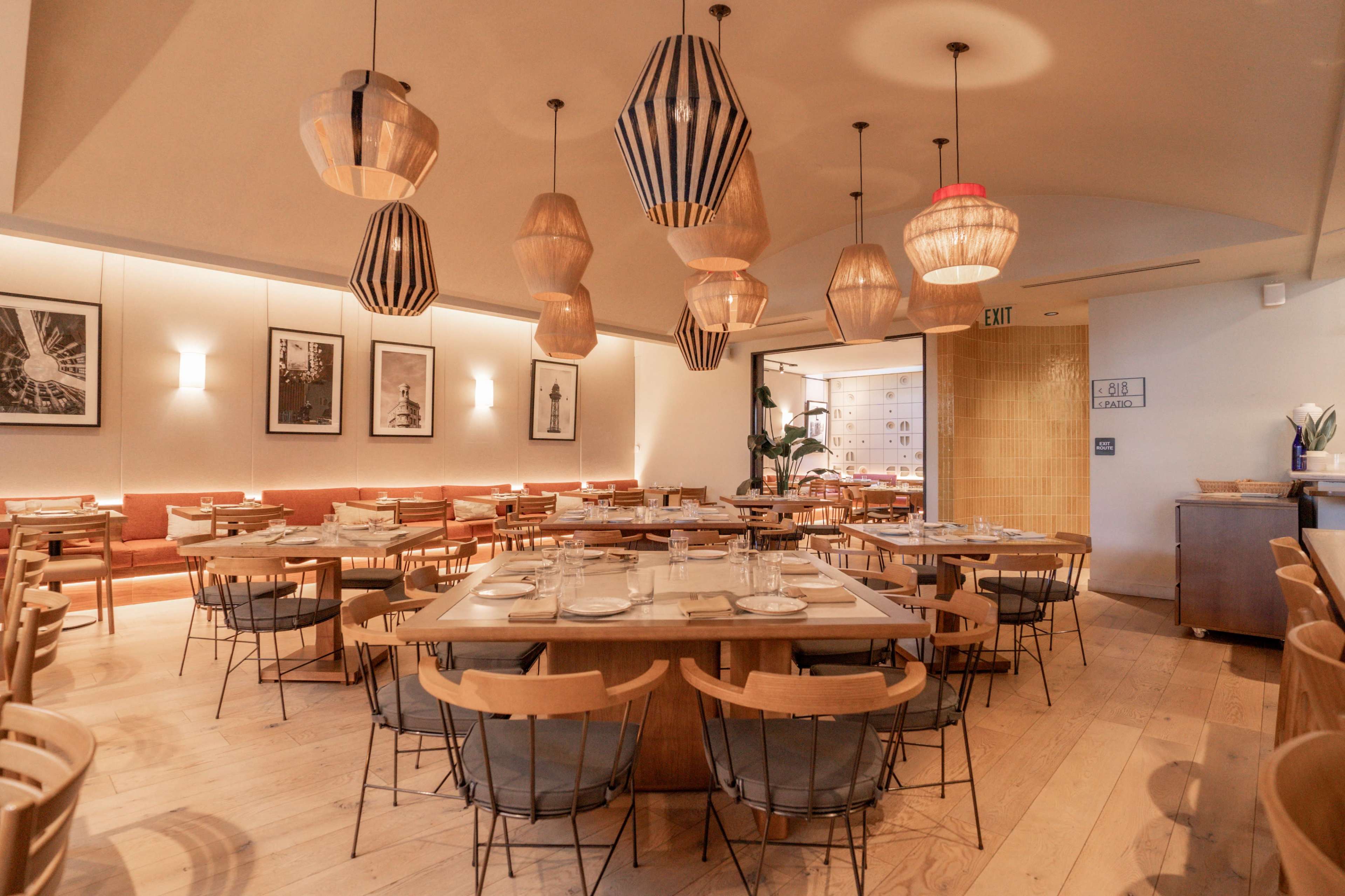 The image shows a modern restaurant interior featuring wooden tables and chairs, pendant light fixtures, and framed photographs on the walls.