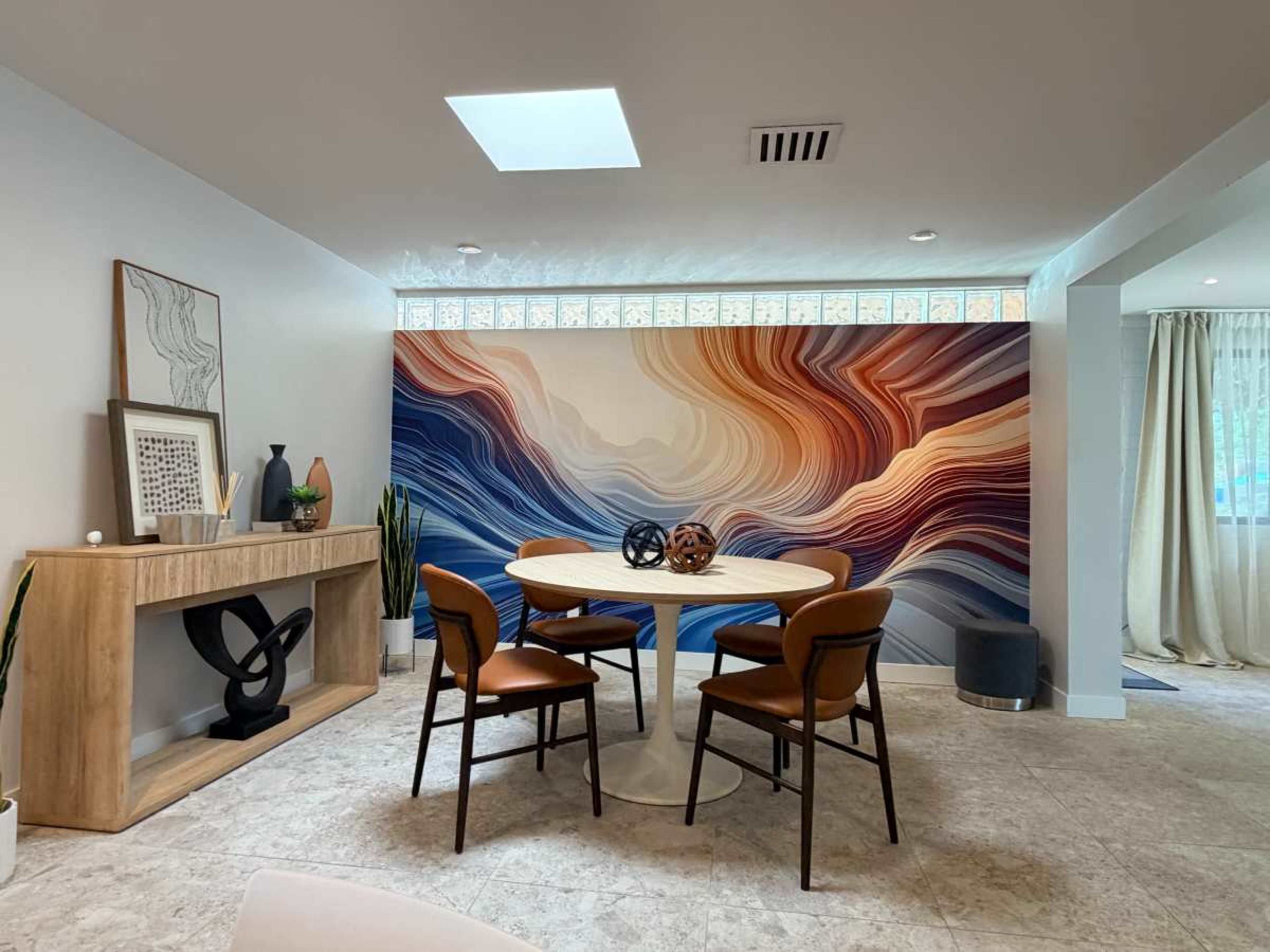 A modern dining area features a round table surrounded by four chairs, with a large abstract mural on the wall and a wooden sideboard.