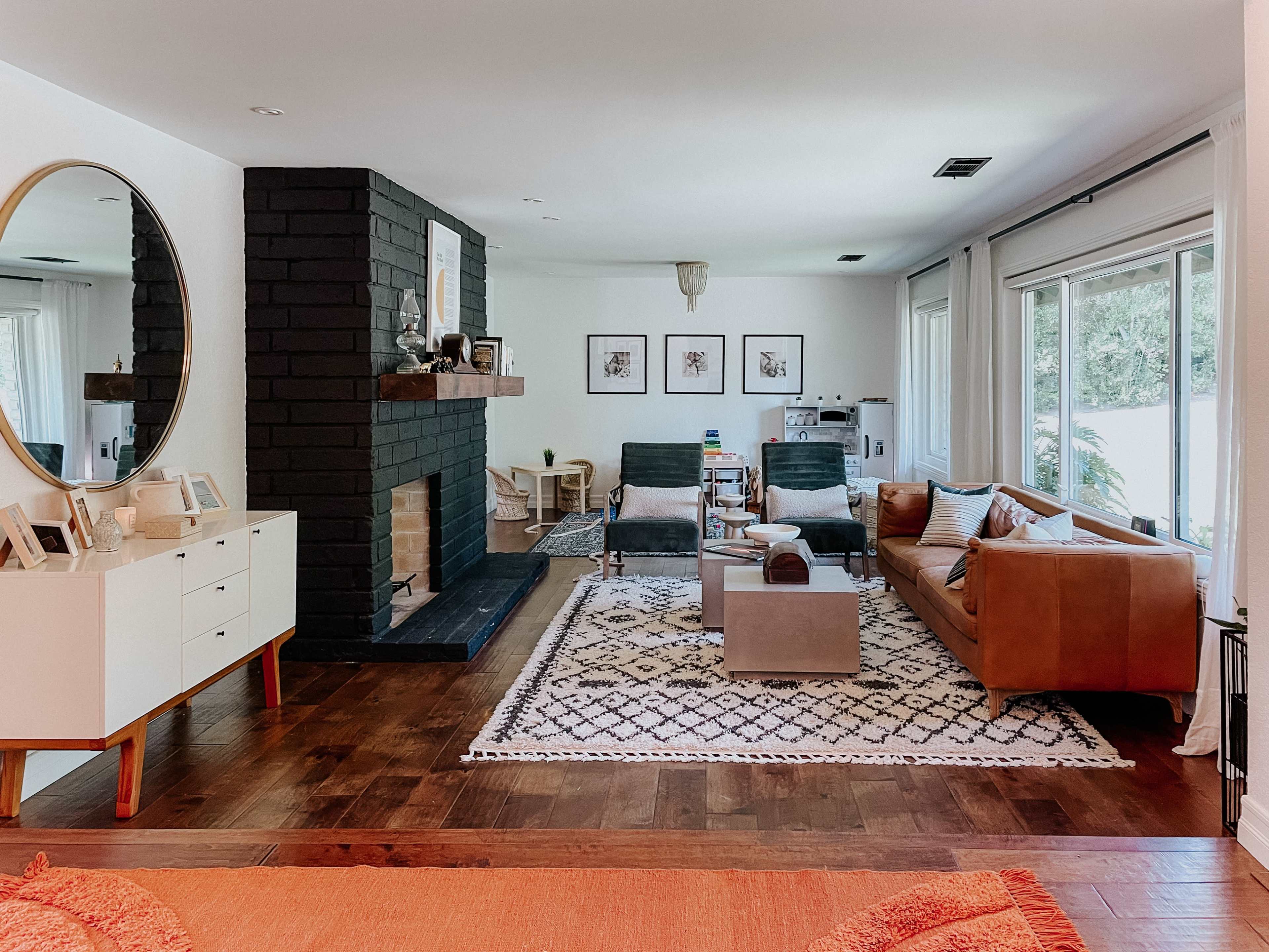 A modern living room featuring a black fireplace, two lounge chairs, a brown sofa, and a large circular mirror on a white wall.
