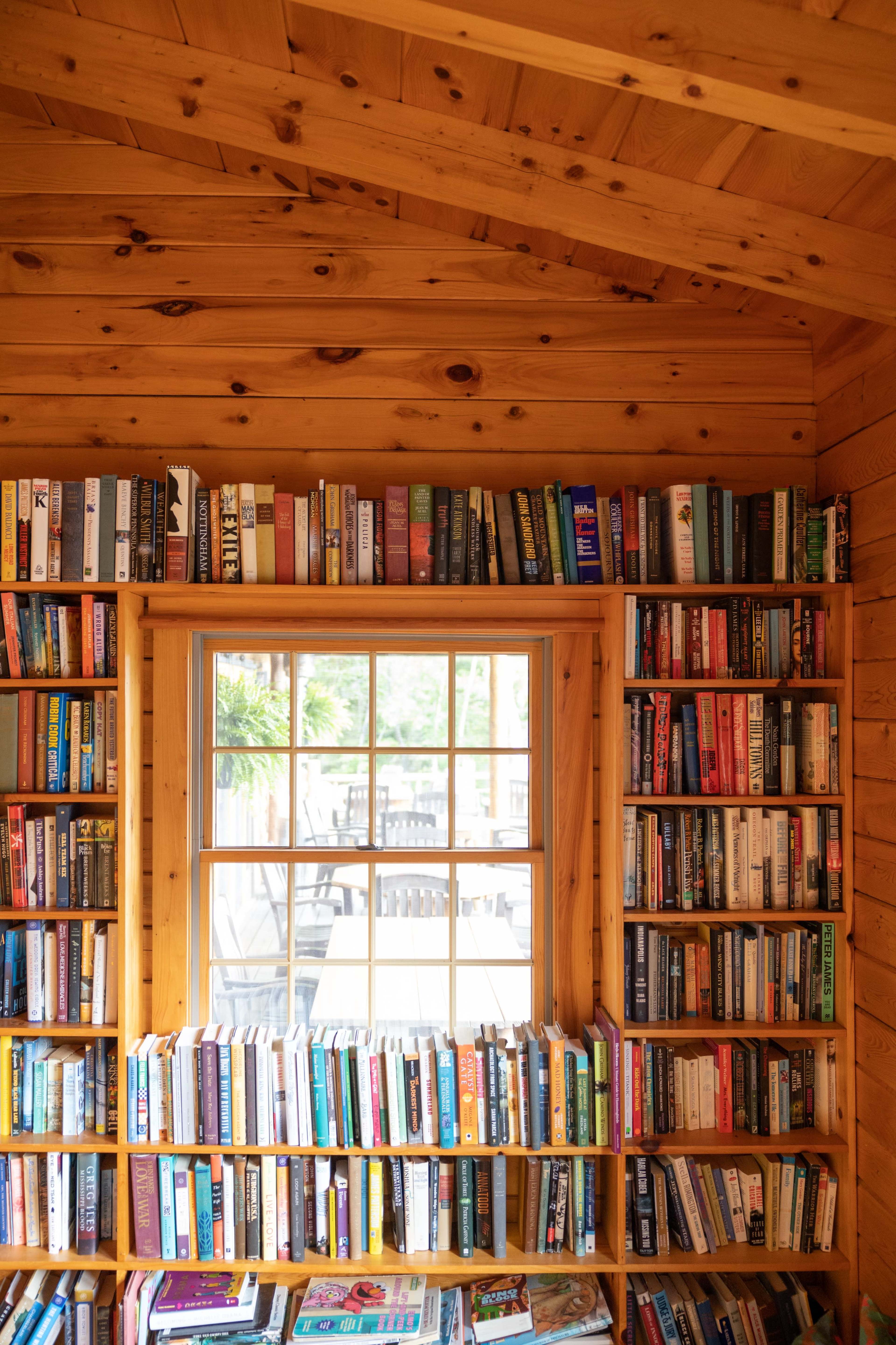 A wooden interior features bookshelves filled with a variety of books surrounding a window.