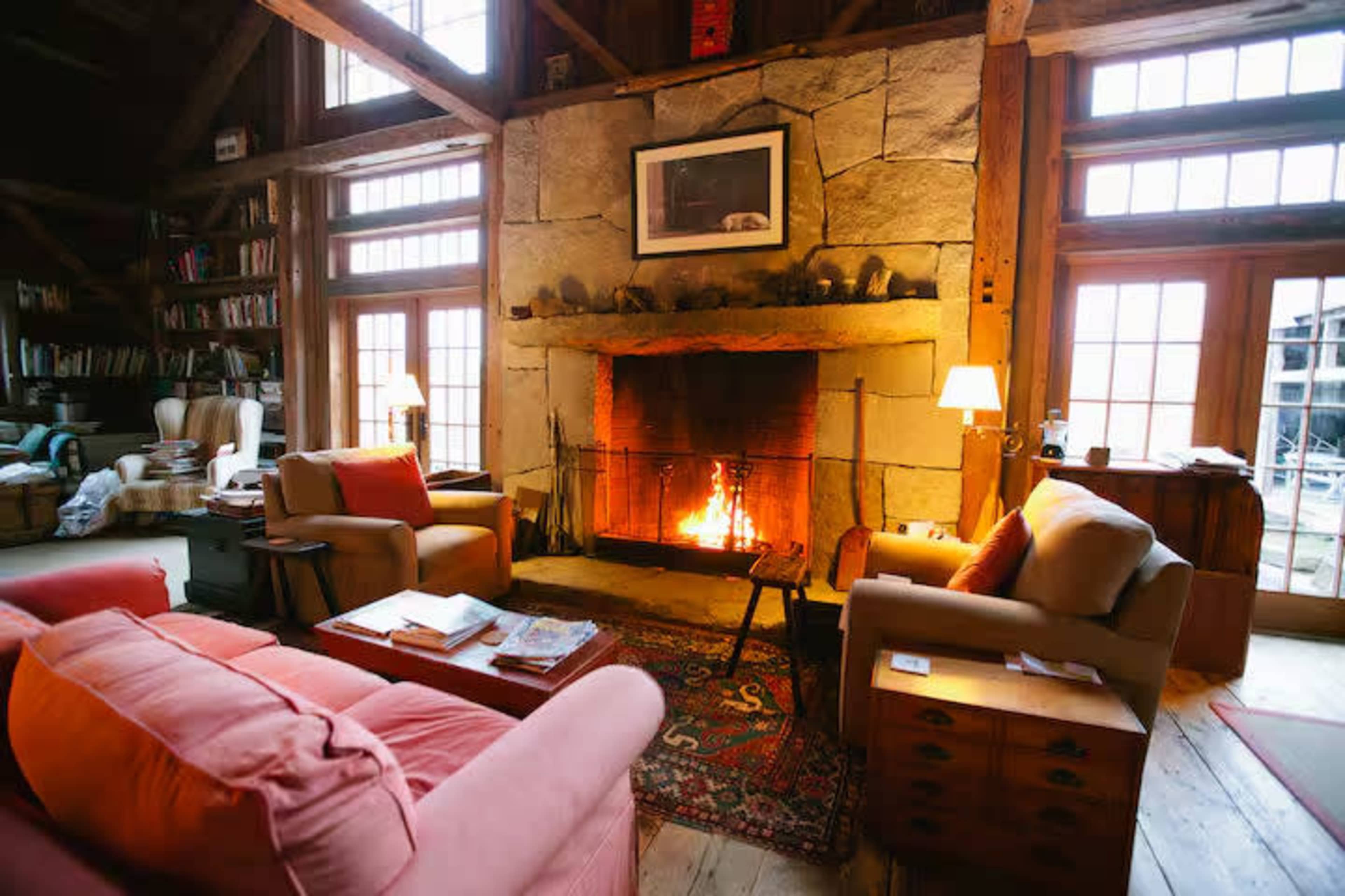 The image shows a cozy living room with a stone fireplace, filled with warm light from the fire, and furnished with comfortable chairs and a rug.