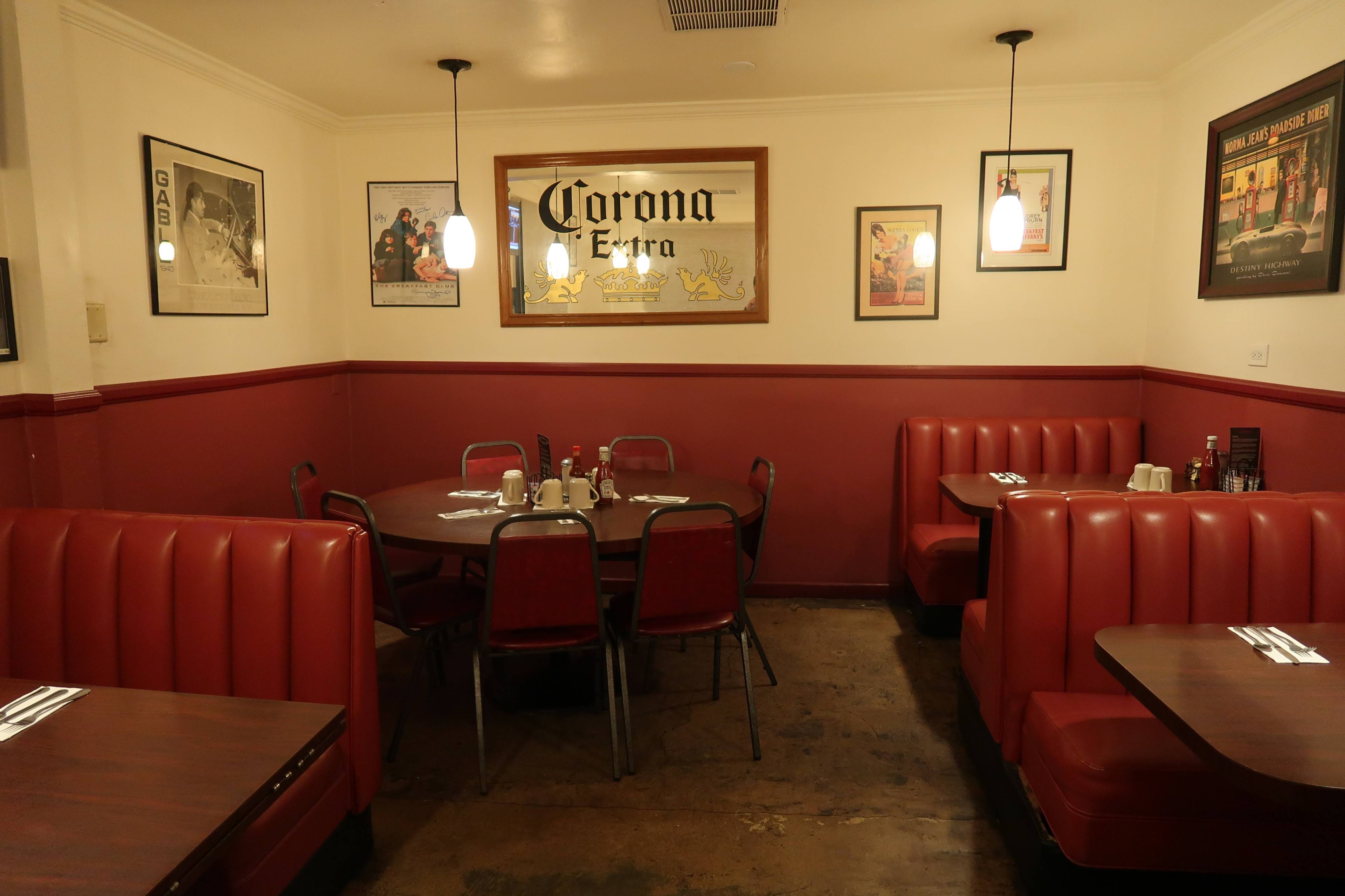 The image shows a cozy restaurant interior with red booths, a round table, and framed posters on the walls.