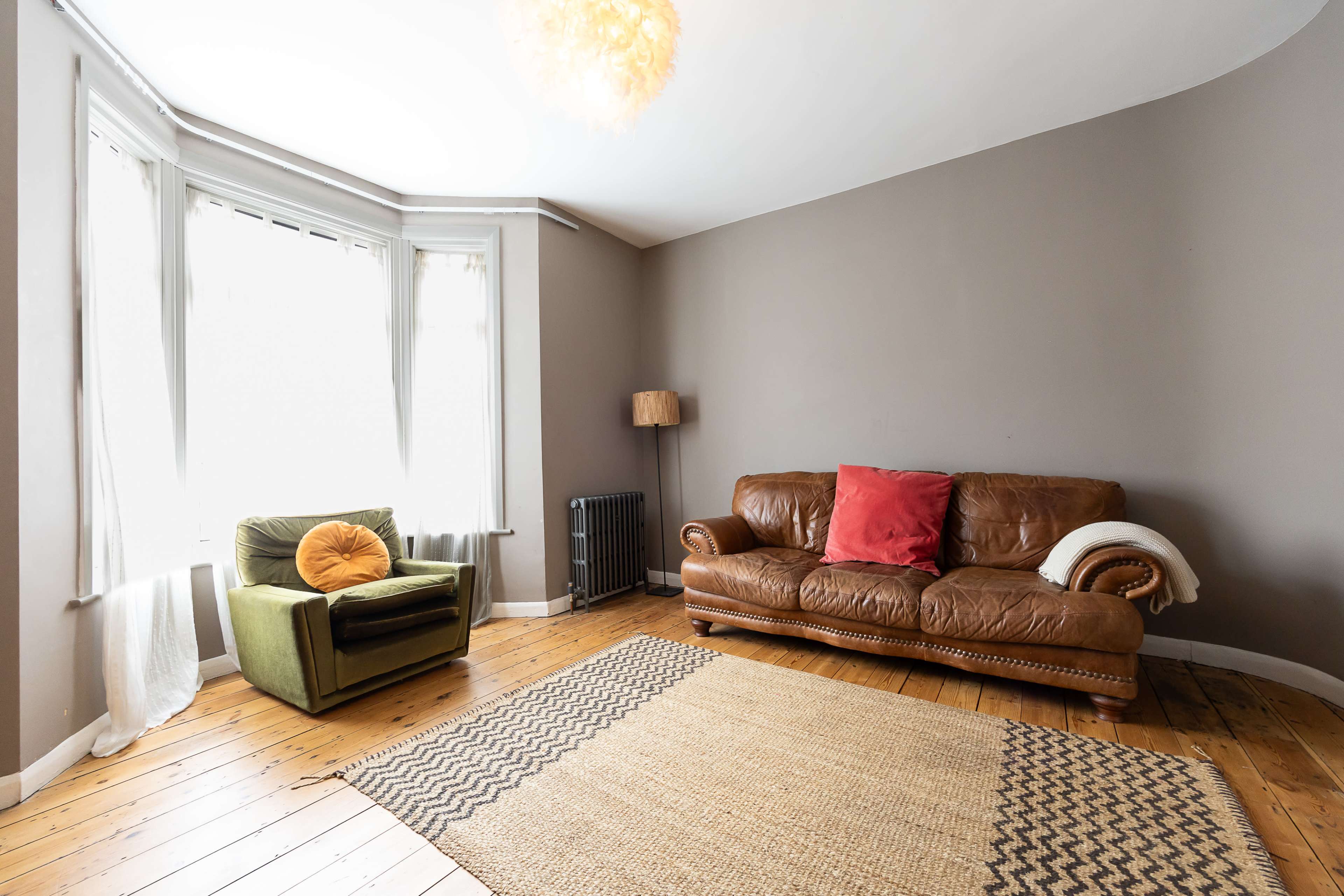 The image shows a living room with a brown leather sofa, a green armchair, a circular rug, and a window allowing natural light.