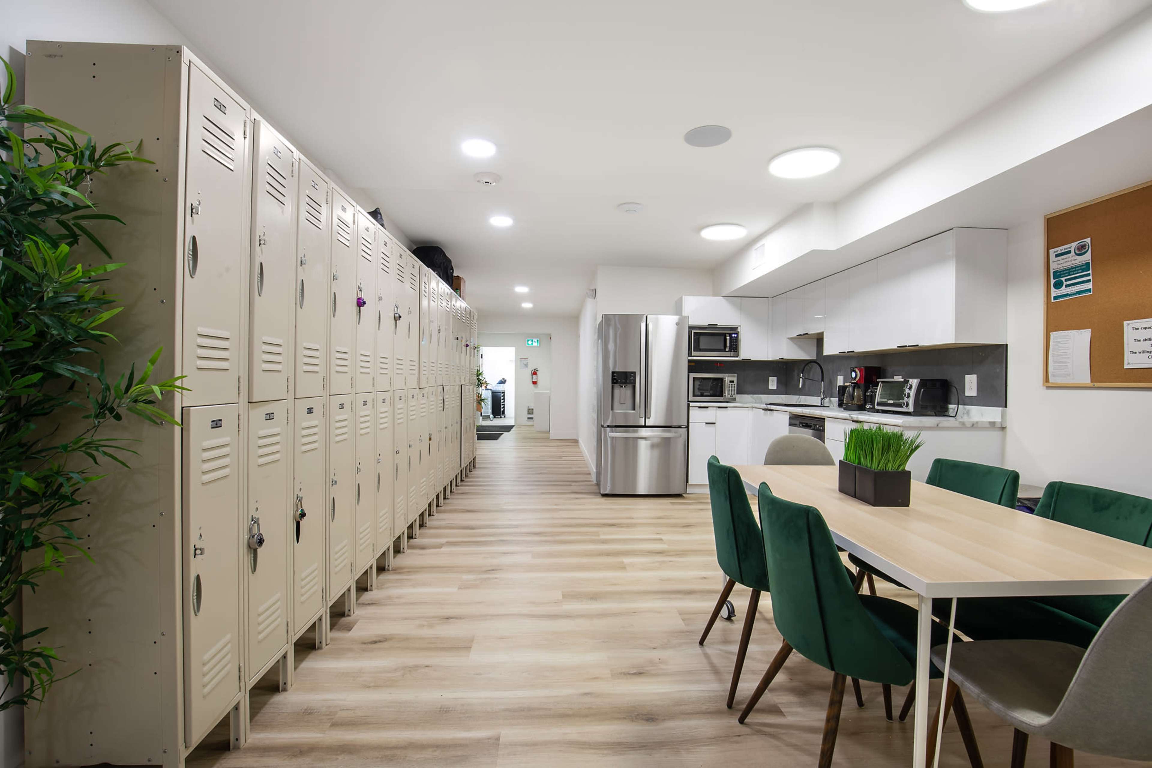 The image shows a modern kitchen and dining area with lockers on one side and a table surrounded by chairs on the other.
