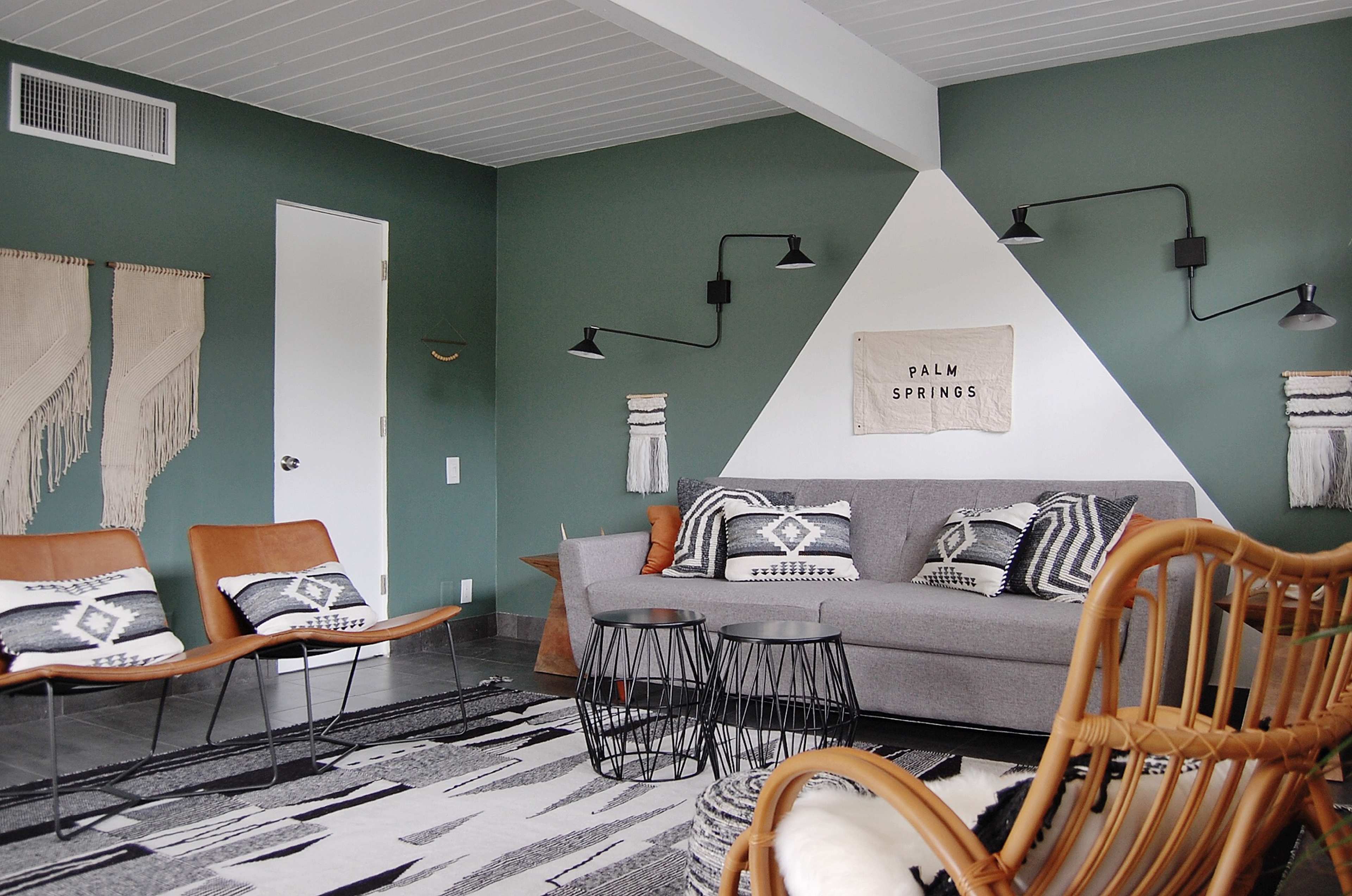 A modern living room featuring a gray sofa, two brown chairs, a black wire coffee table, and a patterned rug against green and white walls.