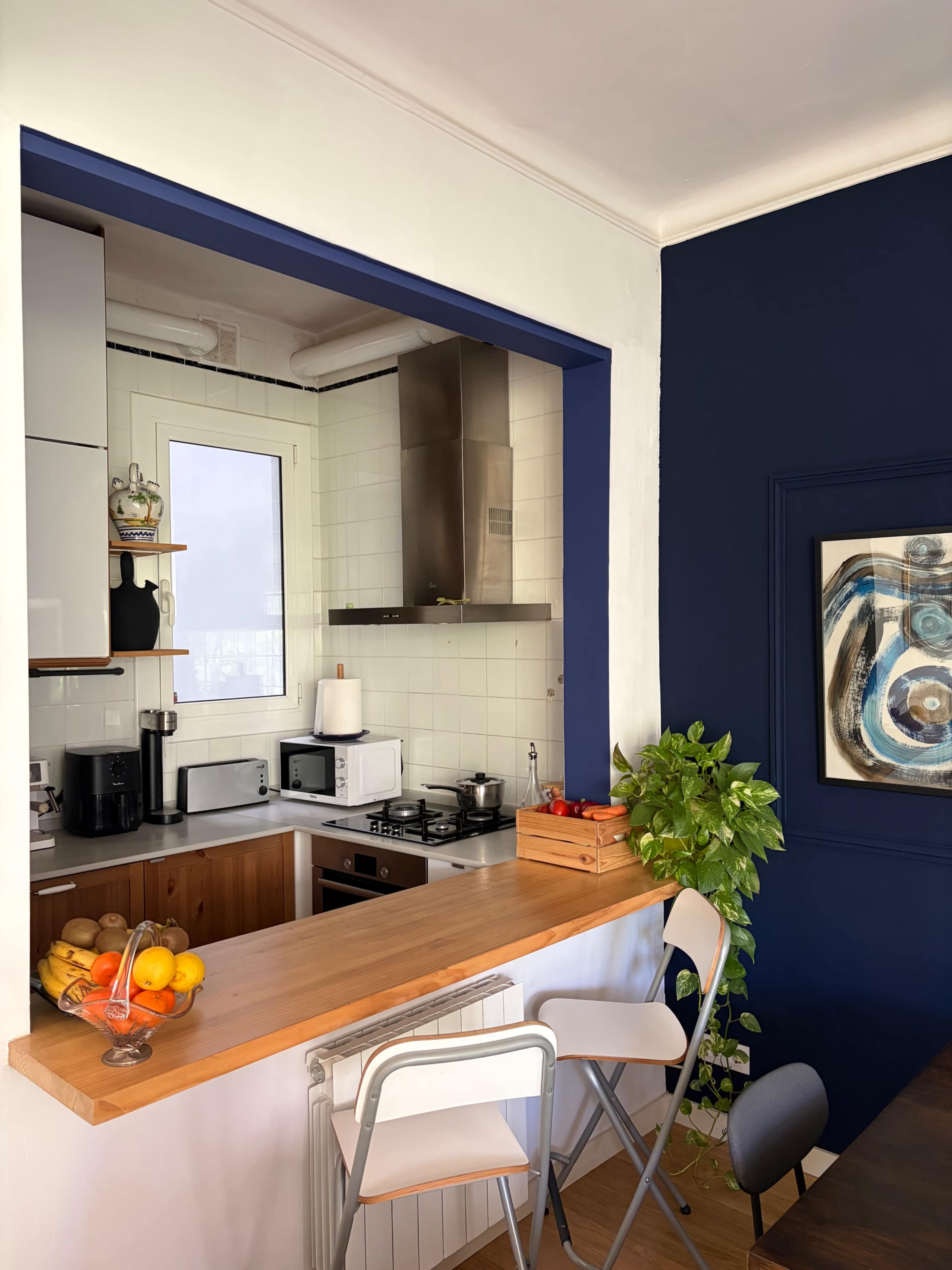 A compact kitchen features a wooden countertop, modern appliances, and a blue accent wall with a piece of artwork.