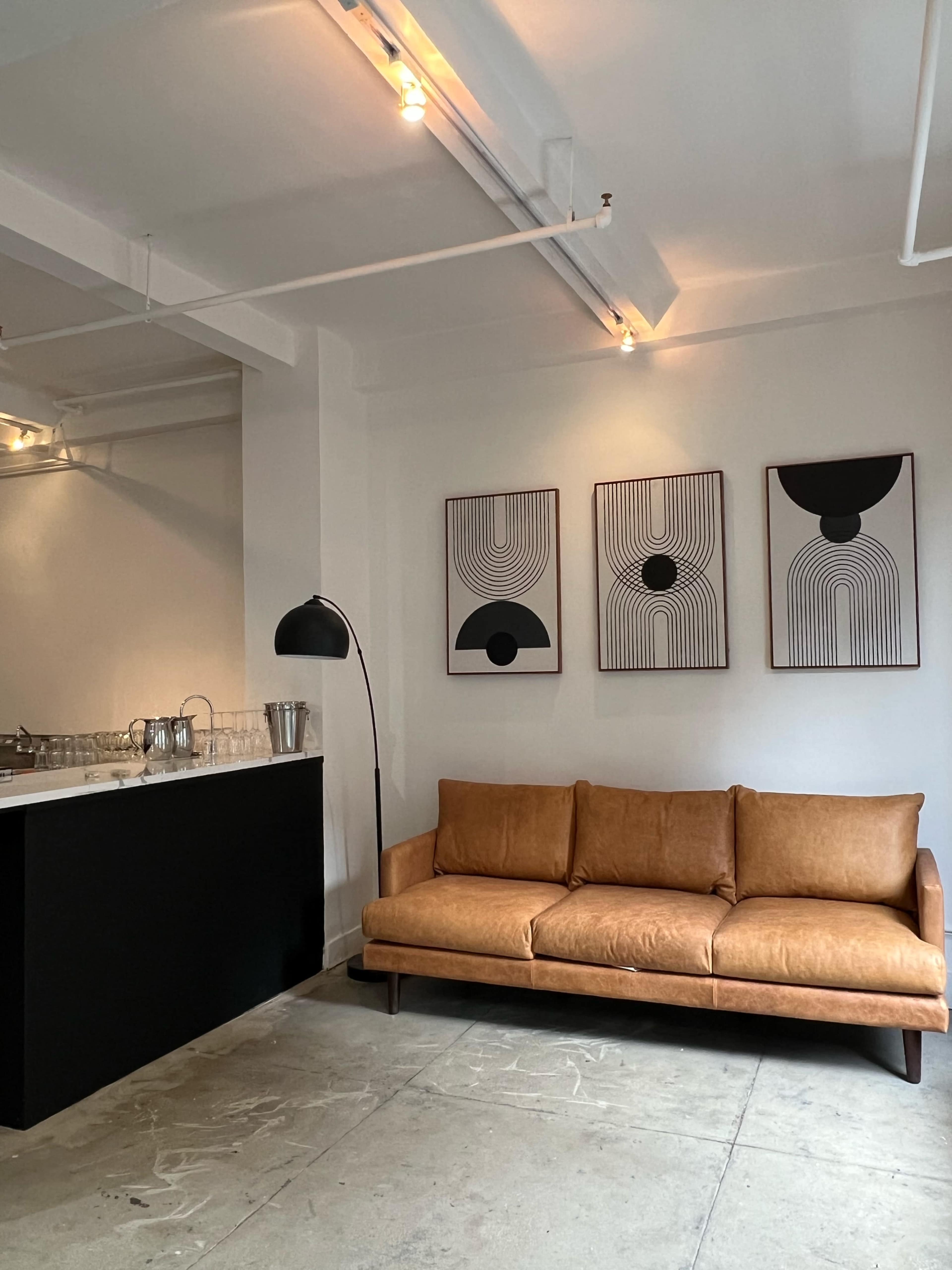 The image shows a modern interior with a brown leather sofa, minimalist artwork on the walls, and a black countertop with glassware.
