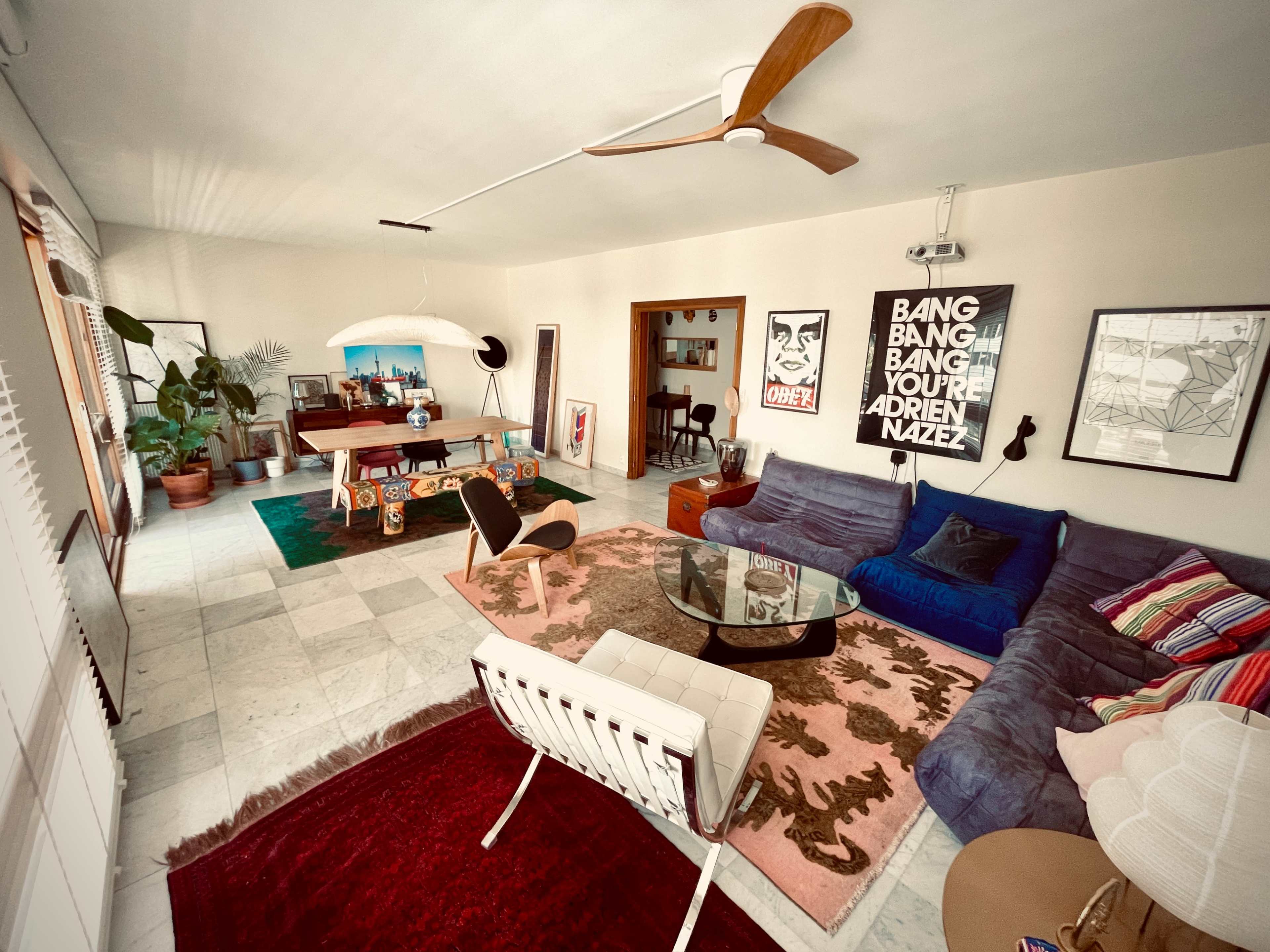 A stylish living room with a blue sectional sofa, a glass coffee table, and various artworks on the walls.