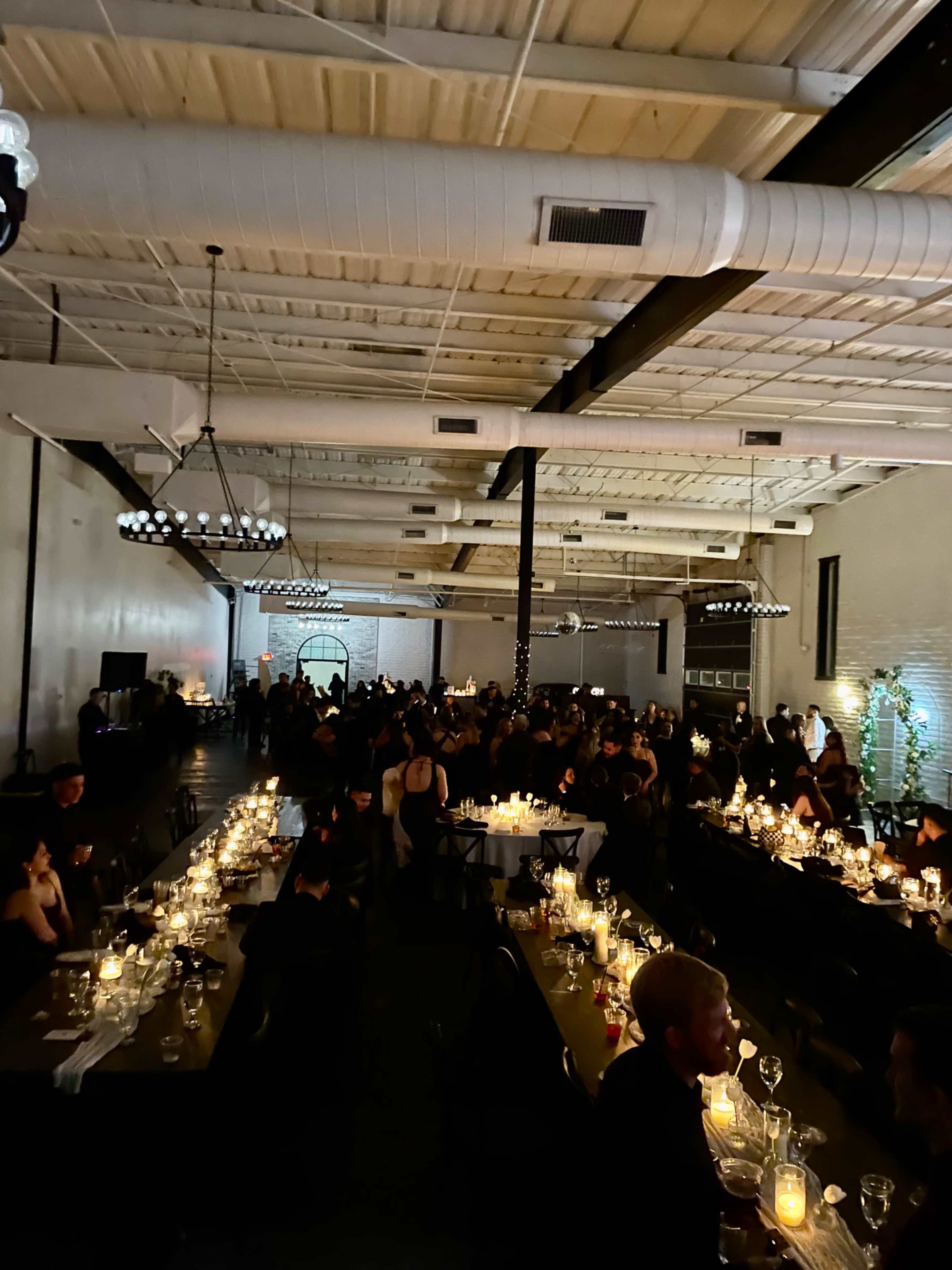 A large indoor venue is filled with guests seated at tables adorned with candles during an evening event.