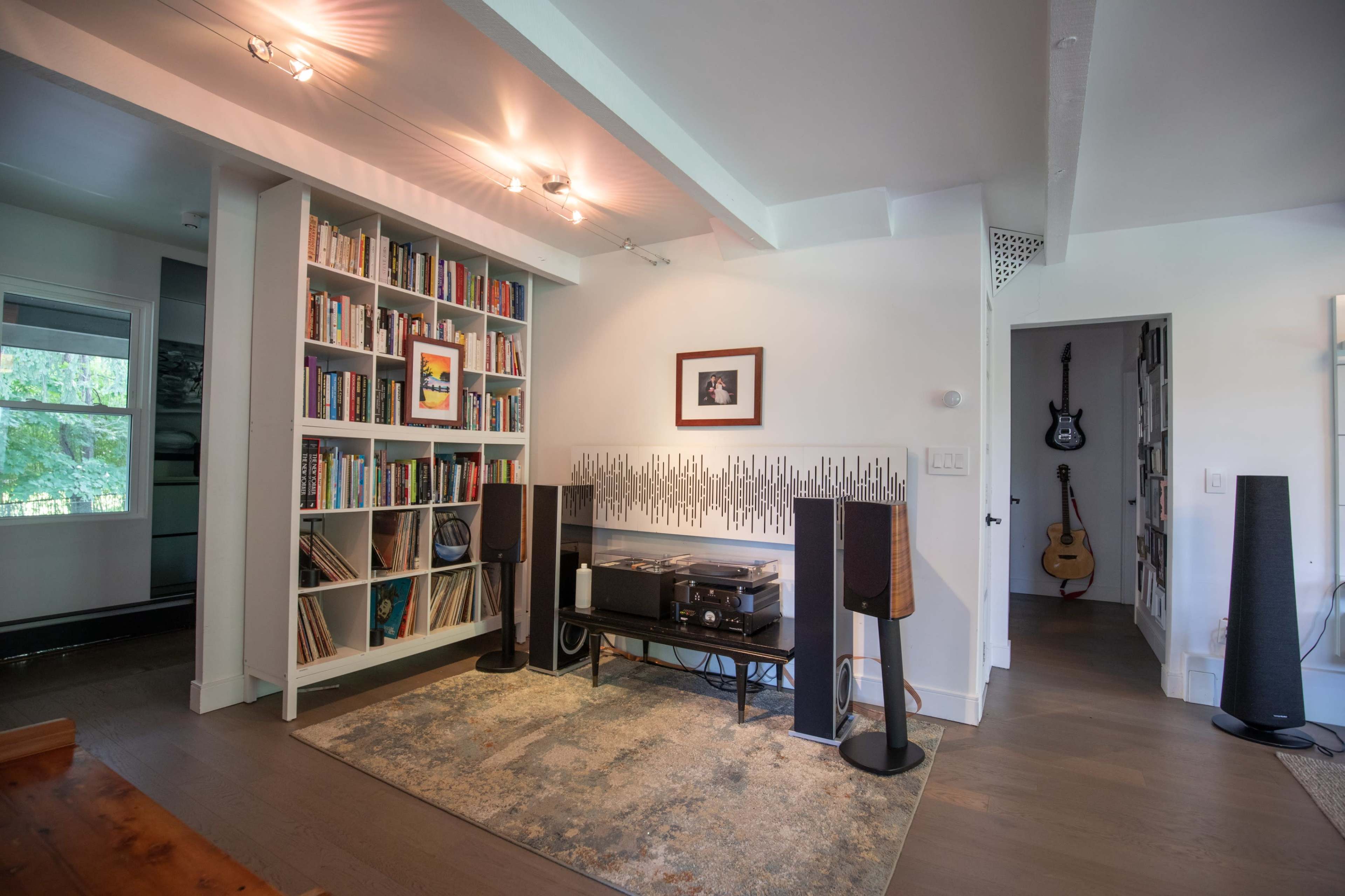 A living room features a bookshelf filled with books, a record player setup, and musical instruments in an adjacent room.