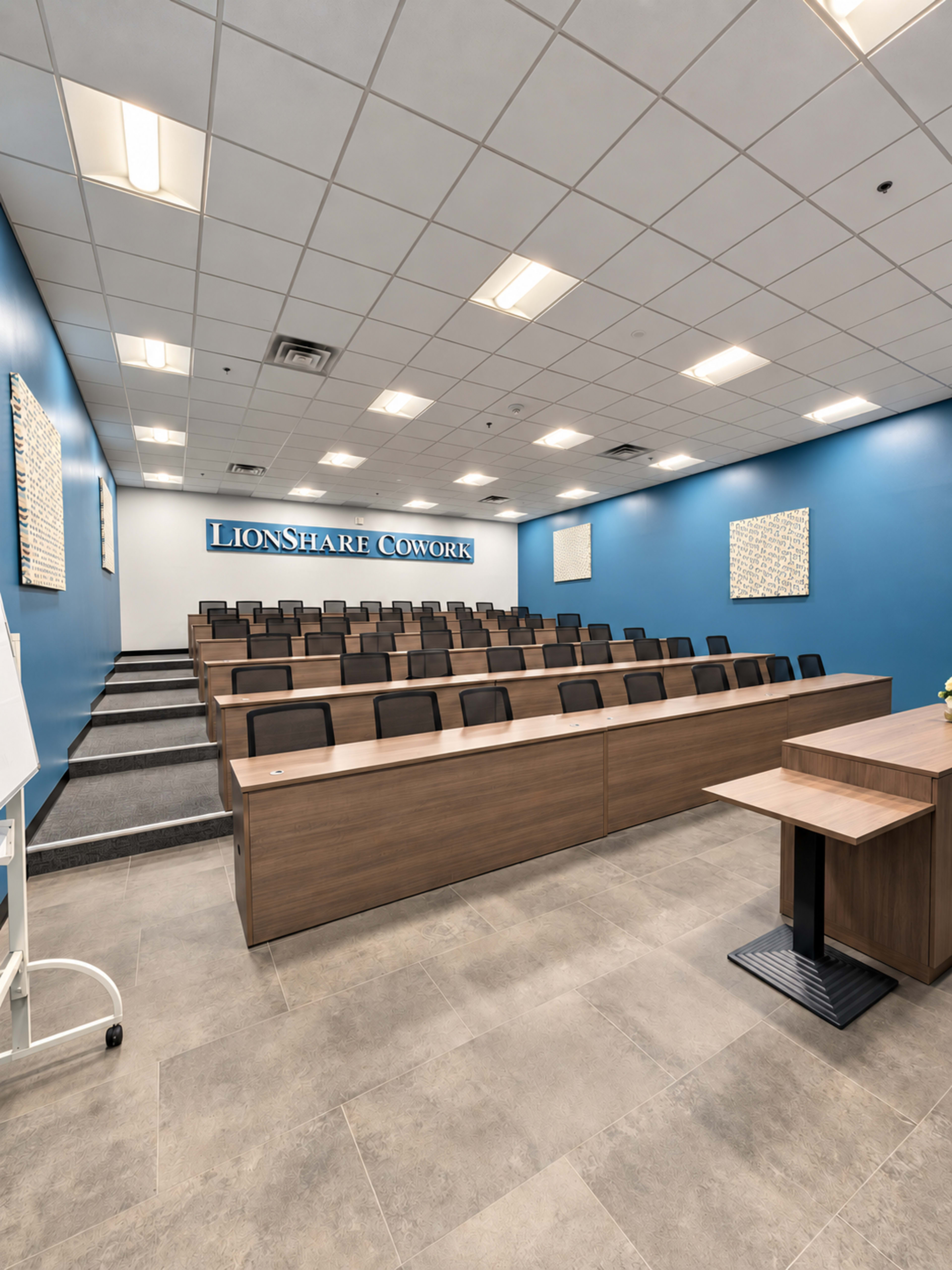 The image shows a spacious conference room with rows of wooden benches and a large blue wall featuring the text "LionShare Cowork."