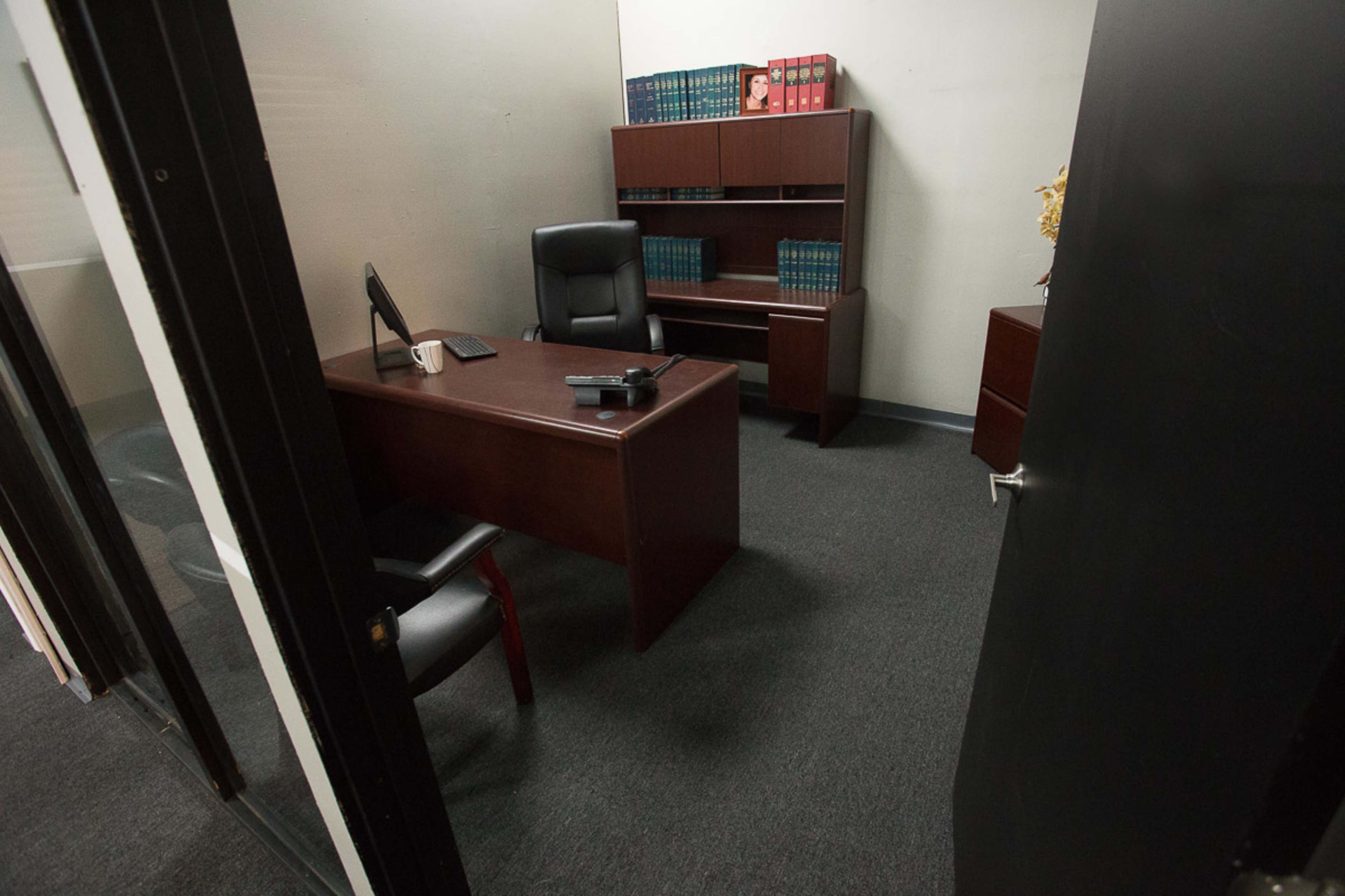 An office with a wooden desk, an office chair, a computer monitor, and a bookshelf filled with books.