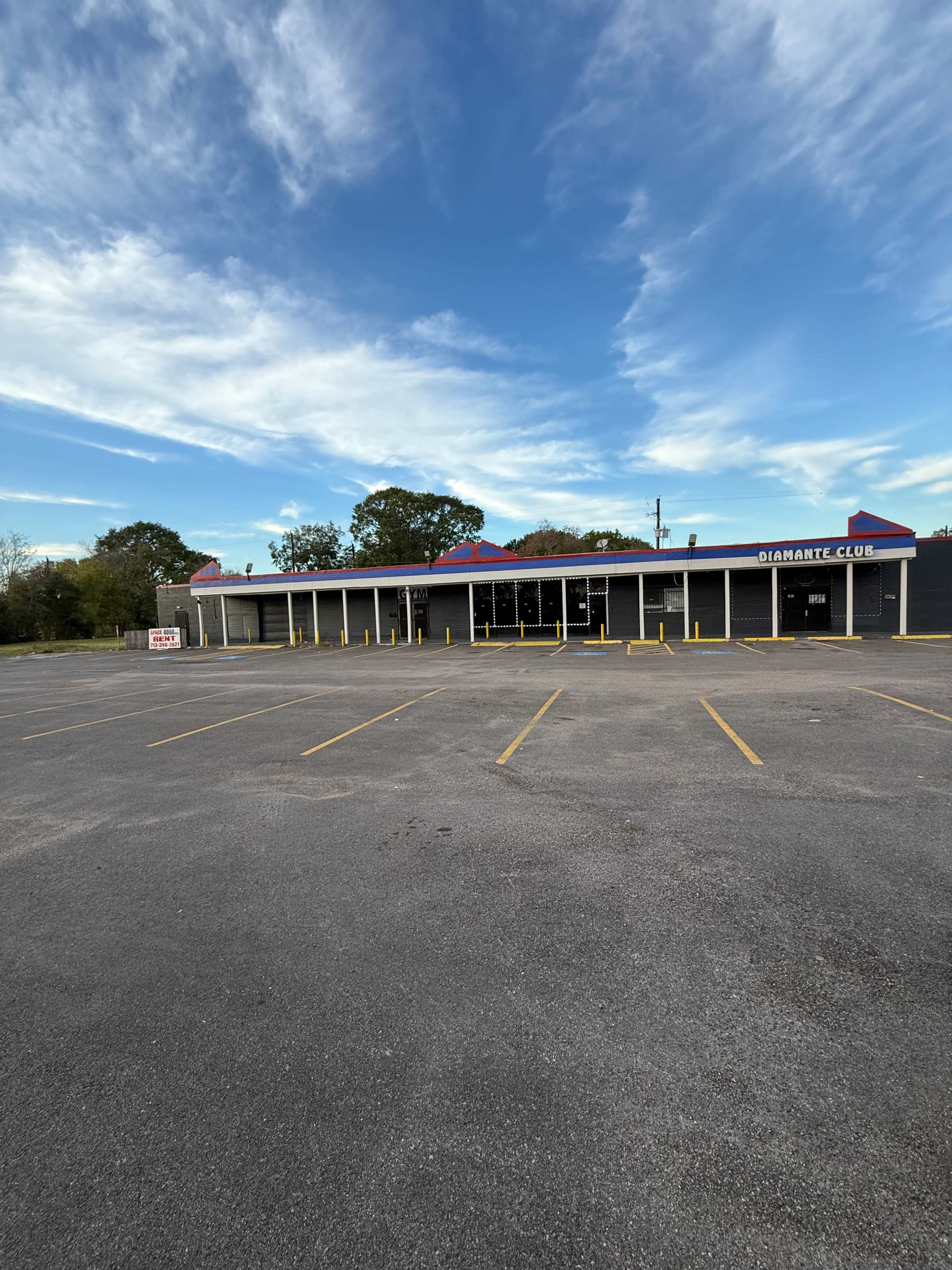 The image shows a large, empty parking lot in front of a single-story commercial building with multiple windows and a sign reading "Gigabyte Club."