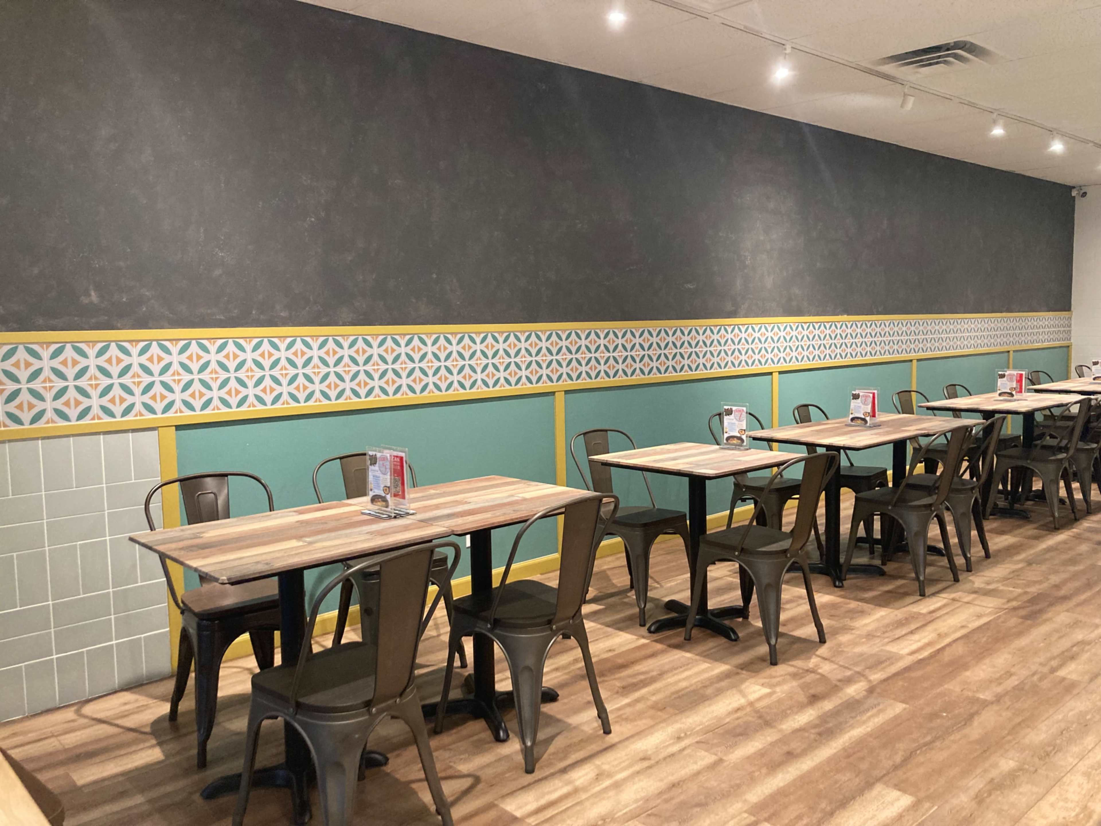 A modern restaurant interior with several wooden tables and metal chairs arranged neatly against a patterned wall.