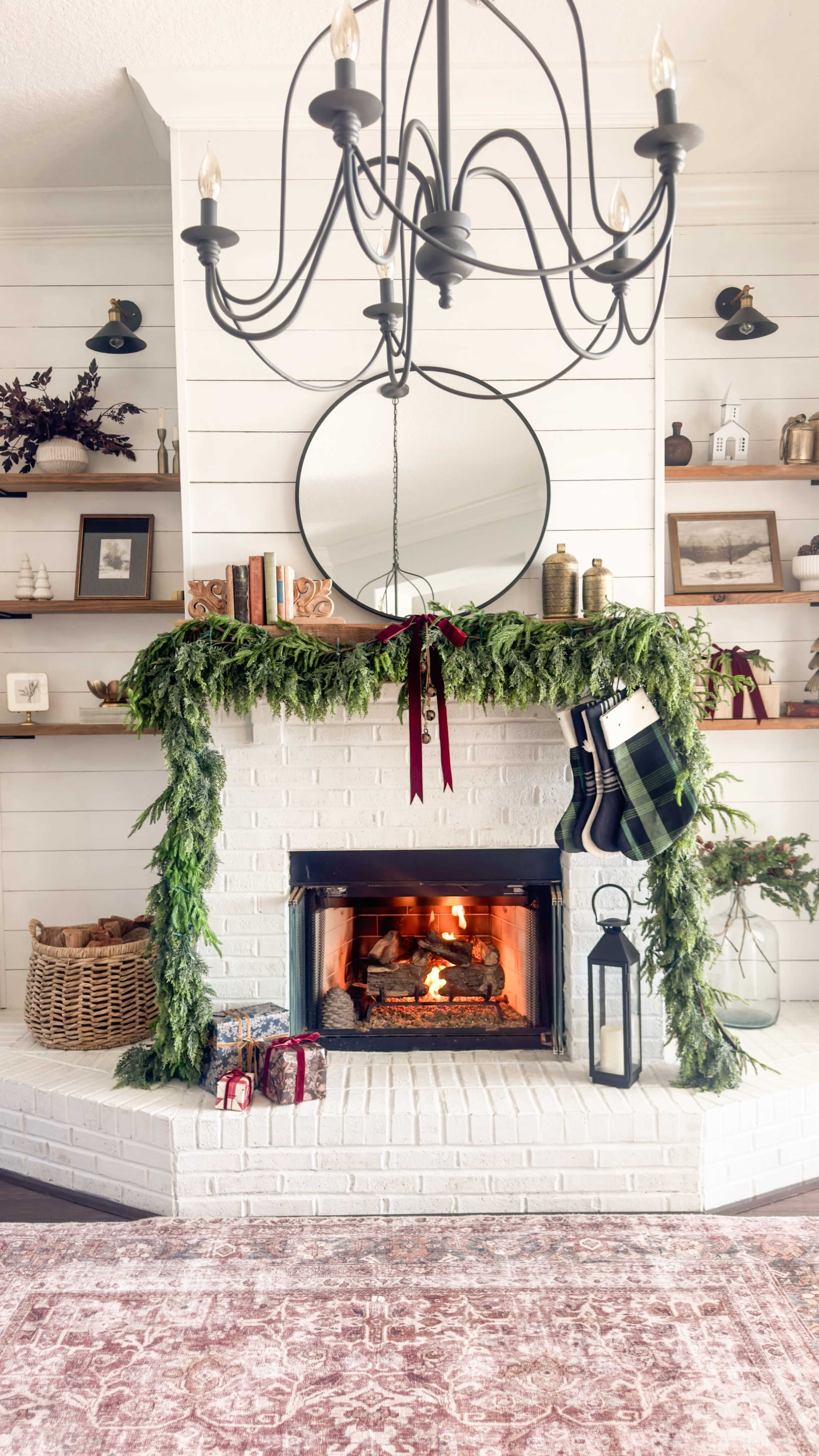 The image features a cozy fireplace adorned with greenery and stockings, surrounded by decorative shelves and a light fixture above.