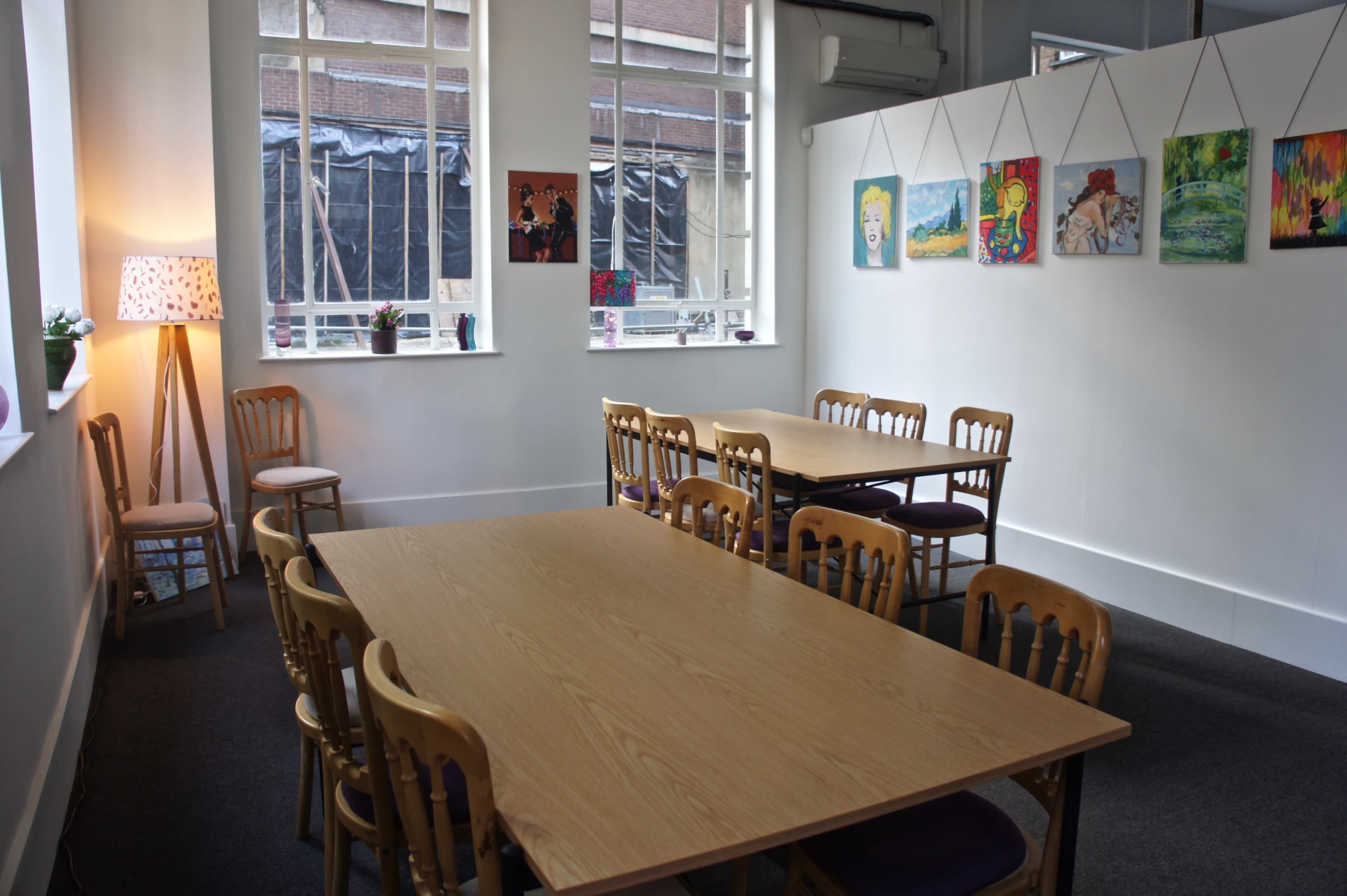 A bright, spacious room with two large tables surrounded by wooden chairs and framed artwork on the walls.