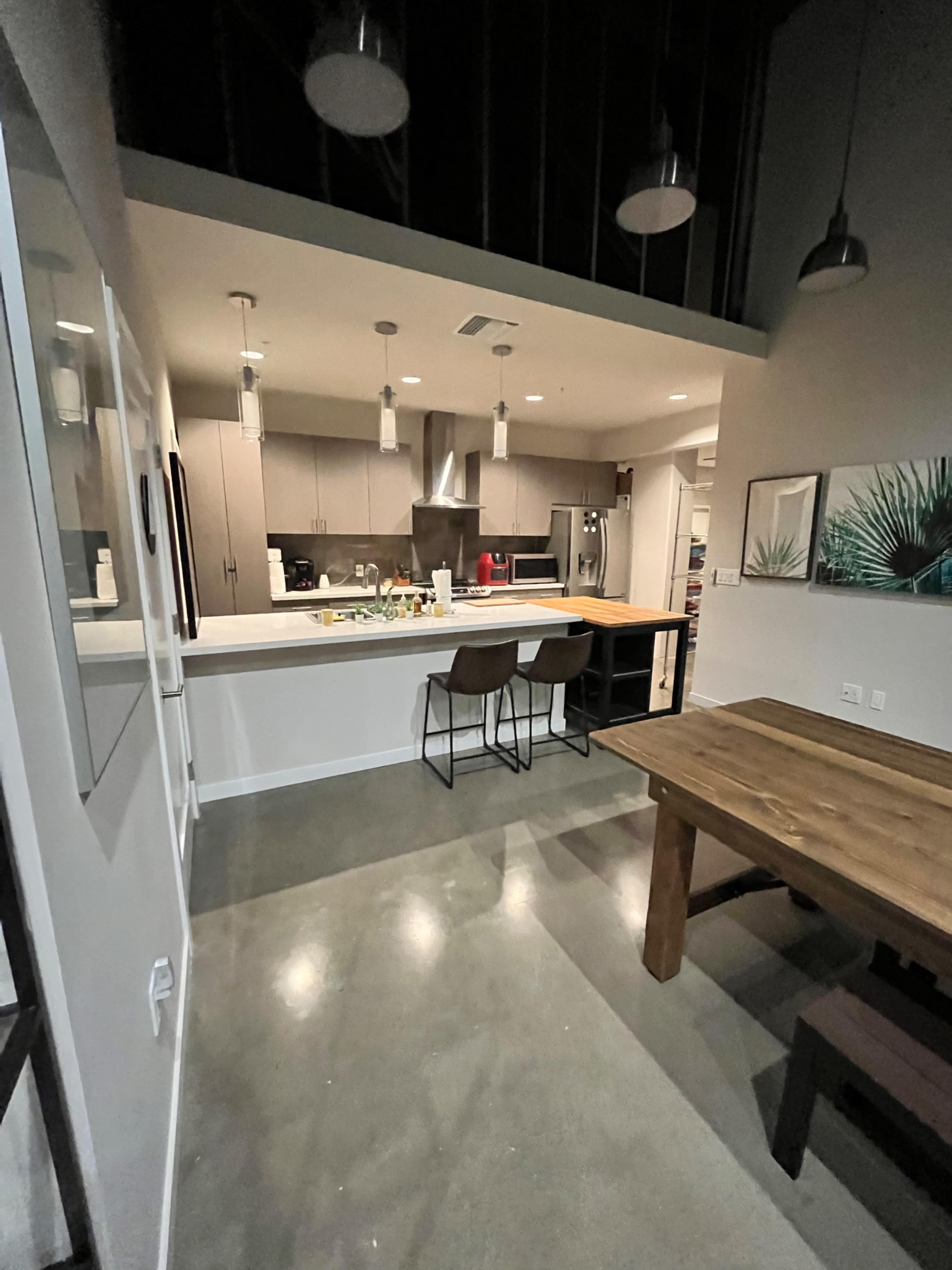 A modern kitchen features a central island with bar stools, stainless steel appliances, and a dining area with a wooden table.