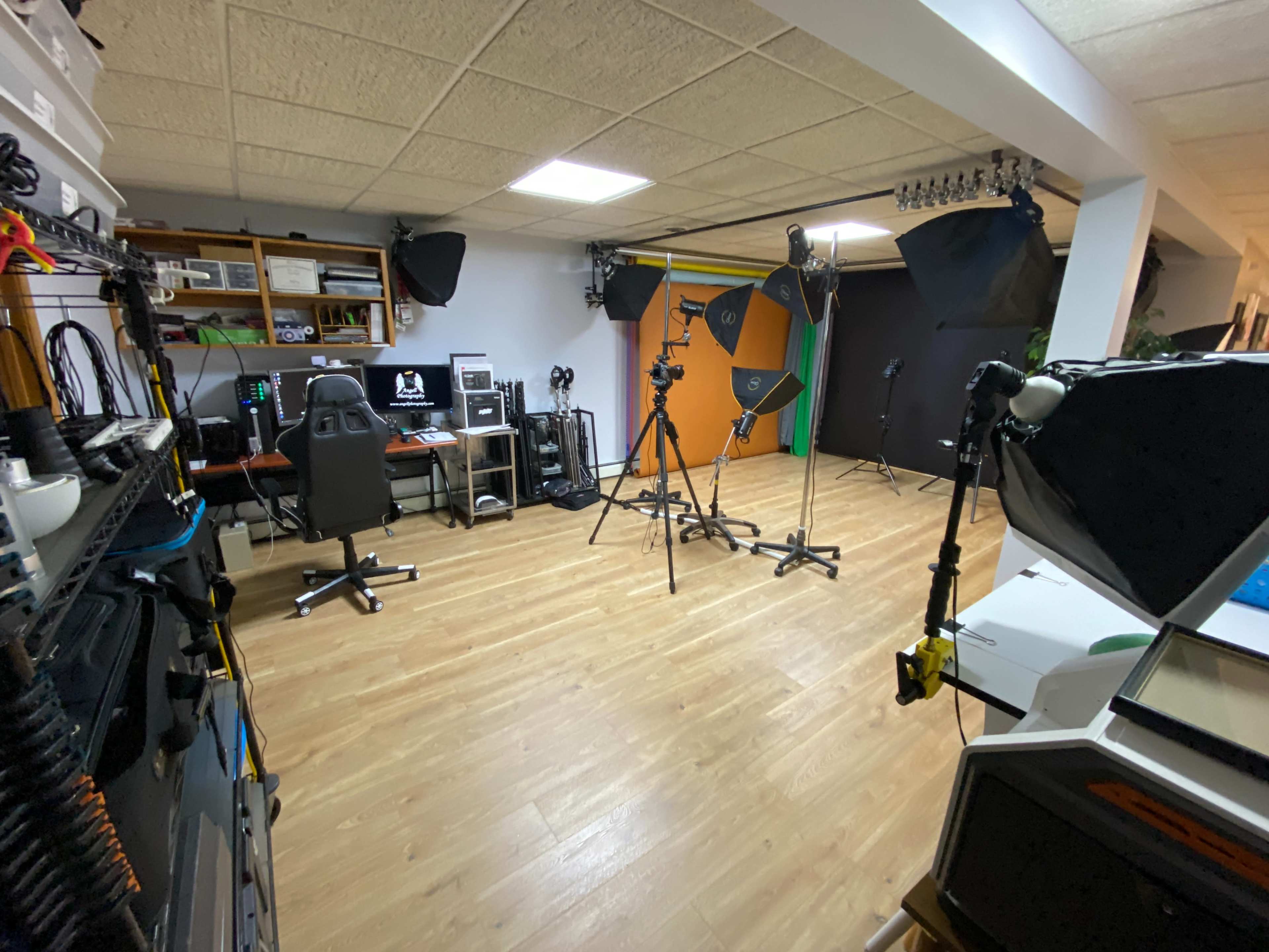The image shows a photography studio equipped with various lighting setups, equipment stands, and computer workstations arranged in a spacious room.