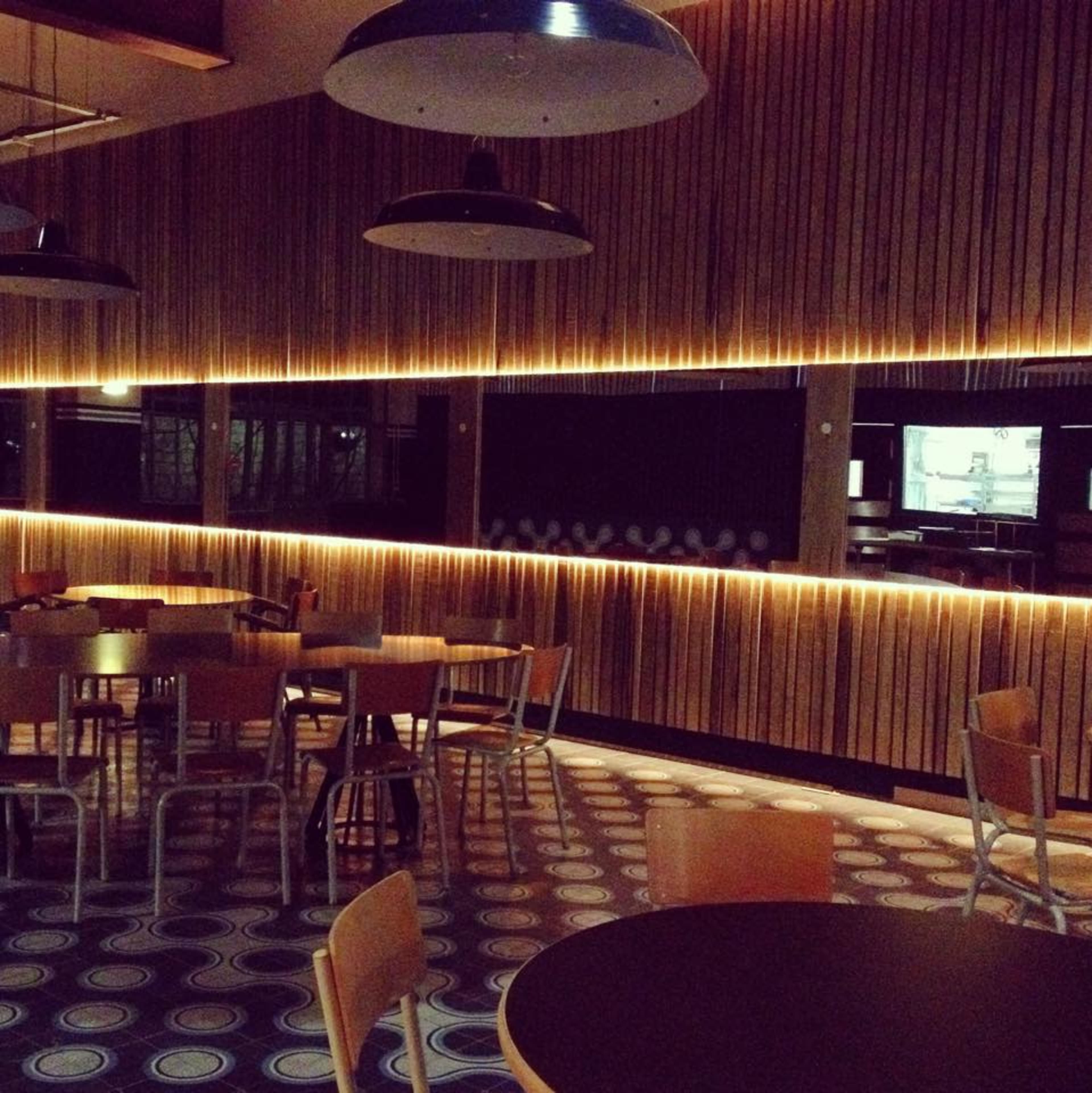 A modern cafe interior features wooden paneling, circular patterned flooring, and empty tables illuminated by warm overhead lighting.