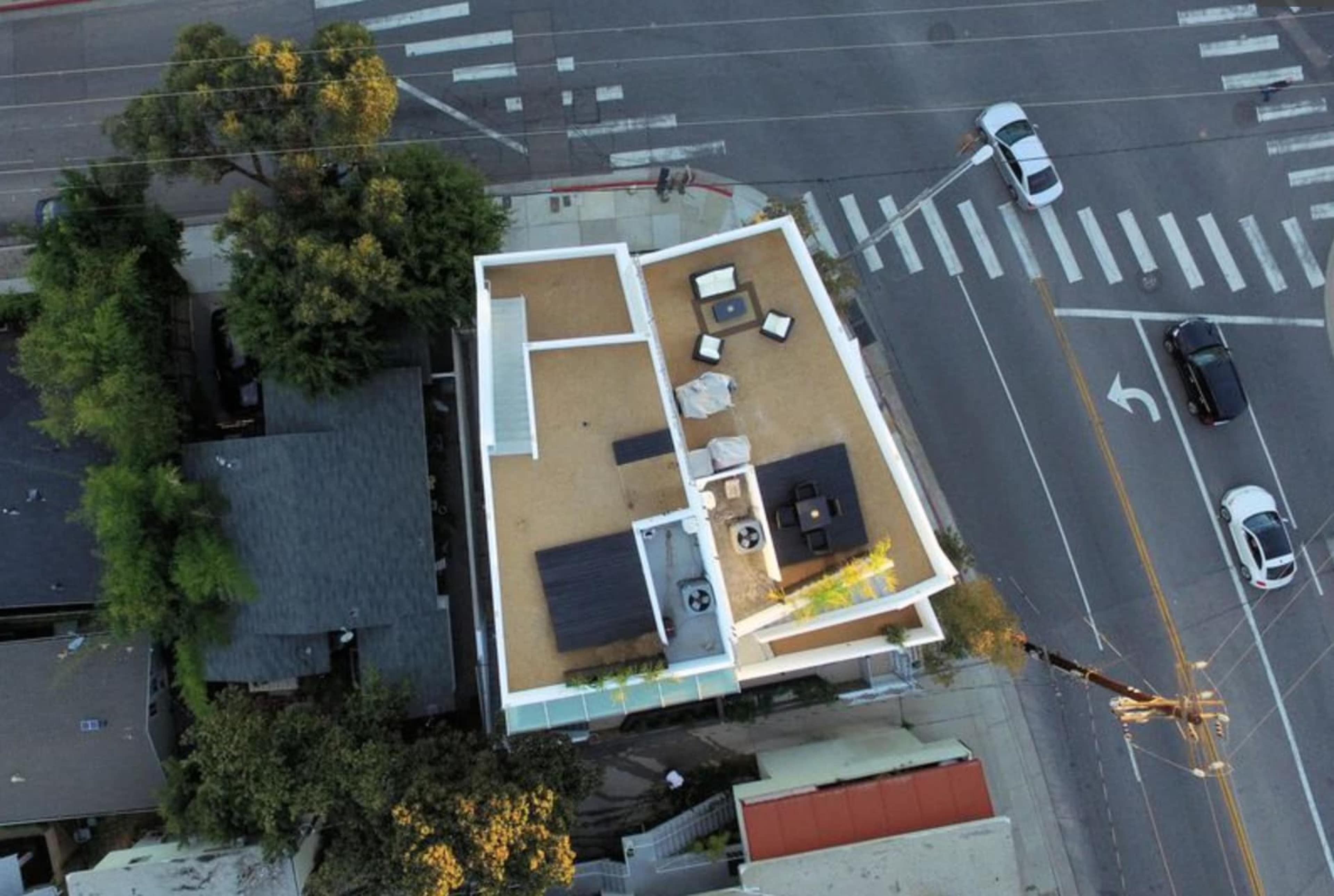 An aerial view of a flat-roofed building with a rooftop patio and surrounding streets.