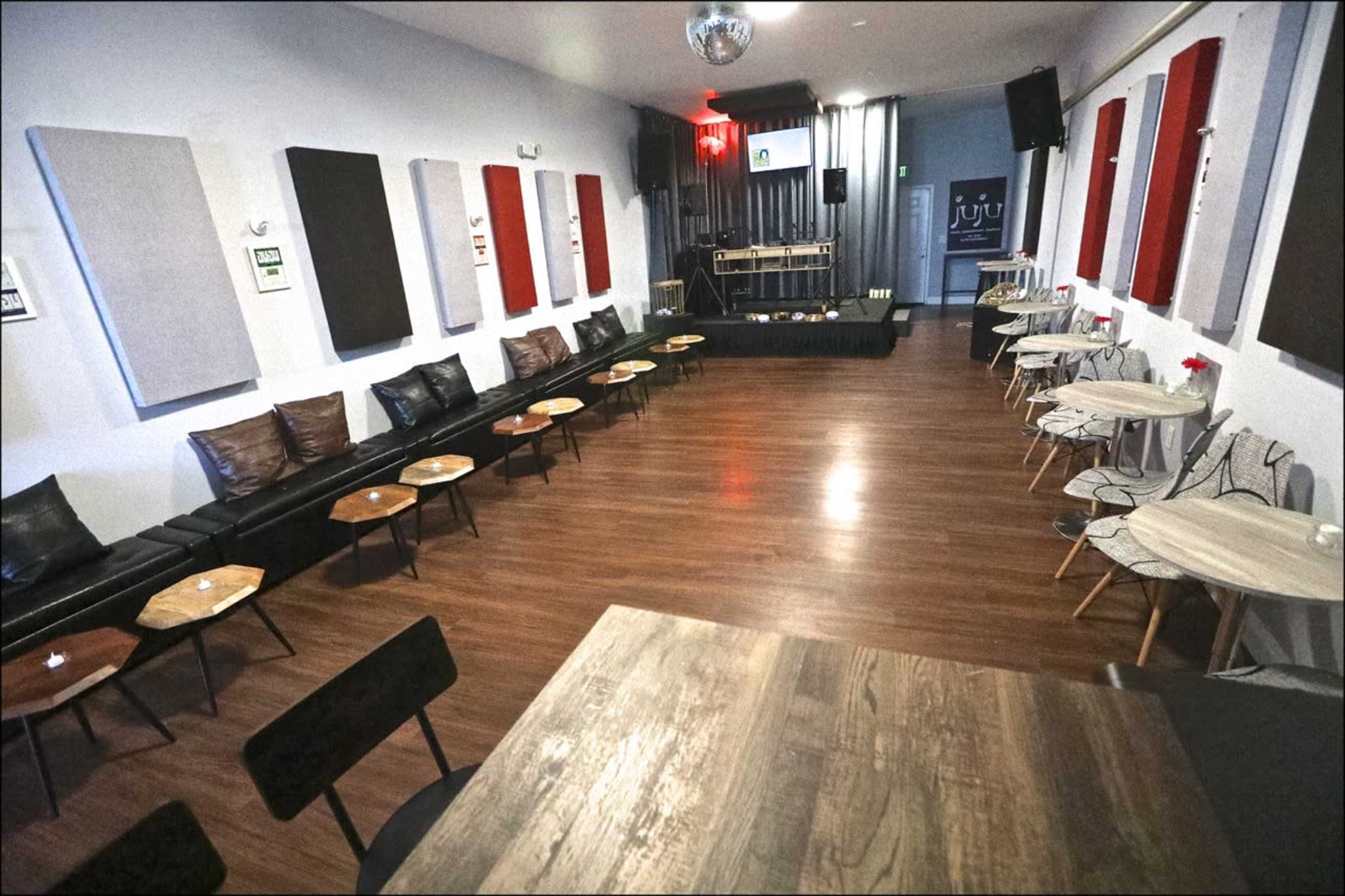 A spacious interior of a lounge or event space with black leather seating, wooden tables, and sound equipment set up at the front.