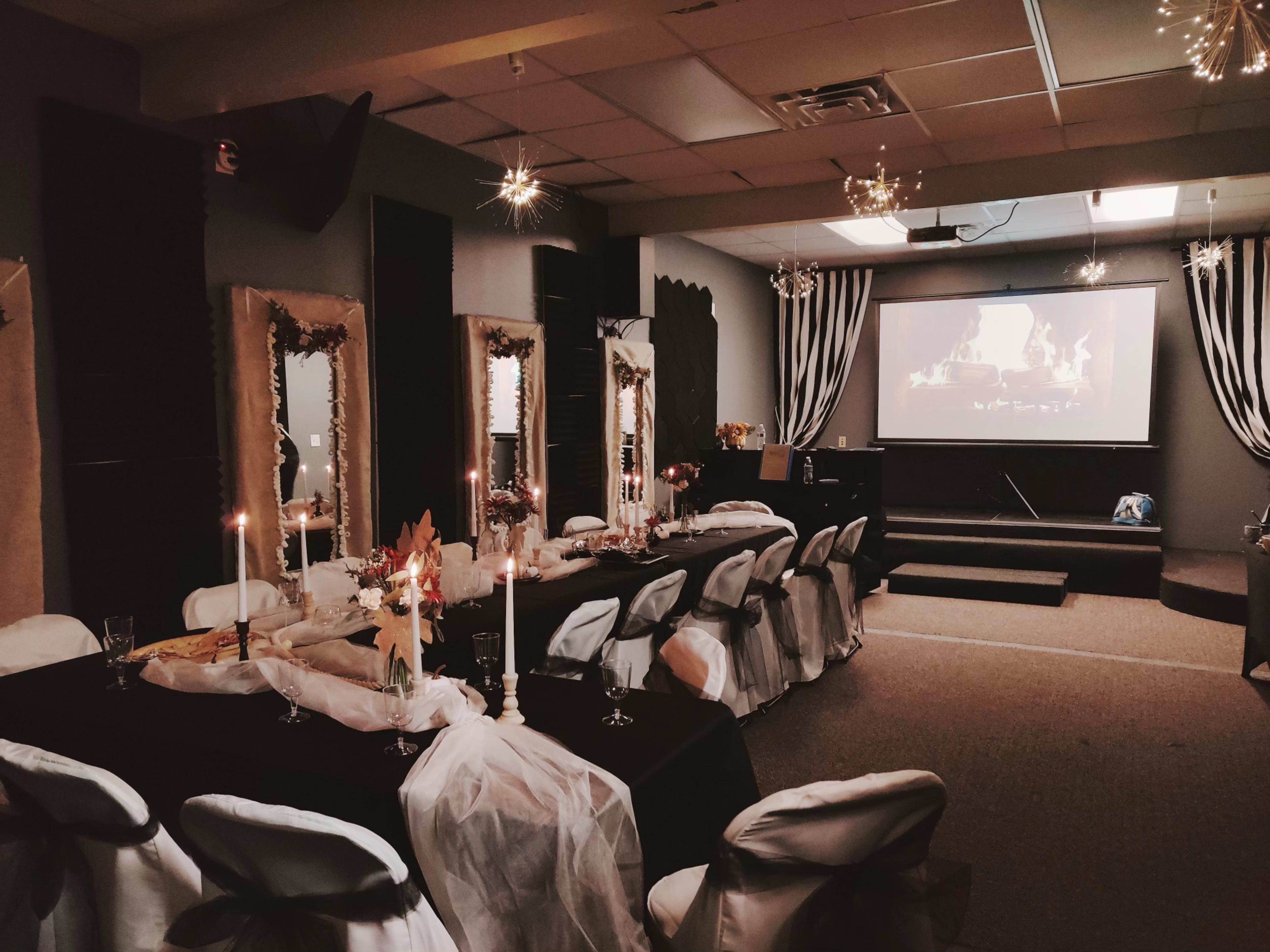 A long banquet table is set with white and black decor, surrounded by chairs, with a projector screen displaying a fire image in the background.