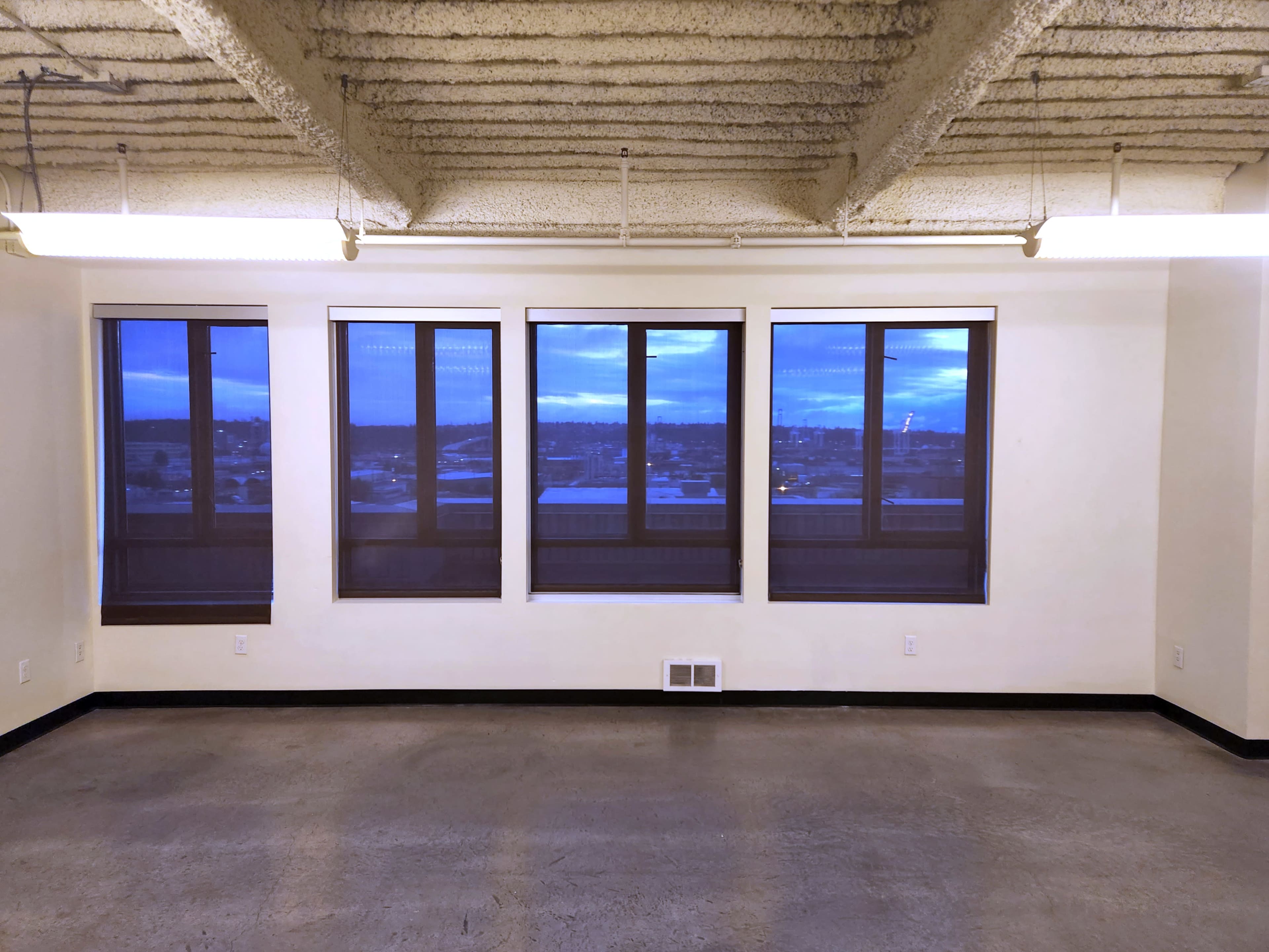 An empty room with concrete flooring and three large windows offering a view of the outside.
