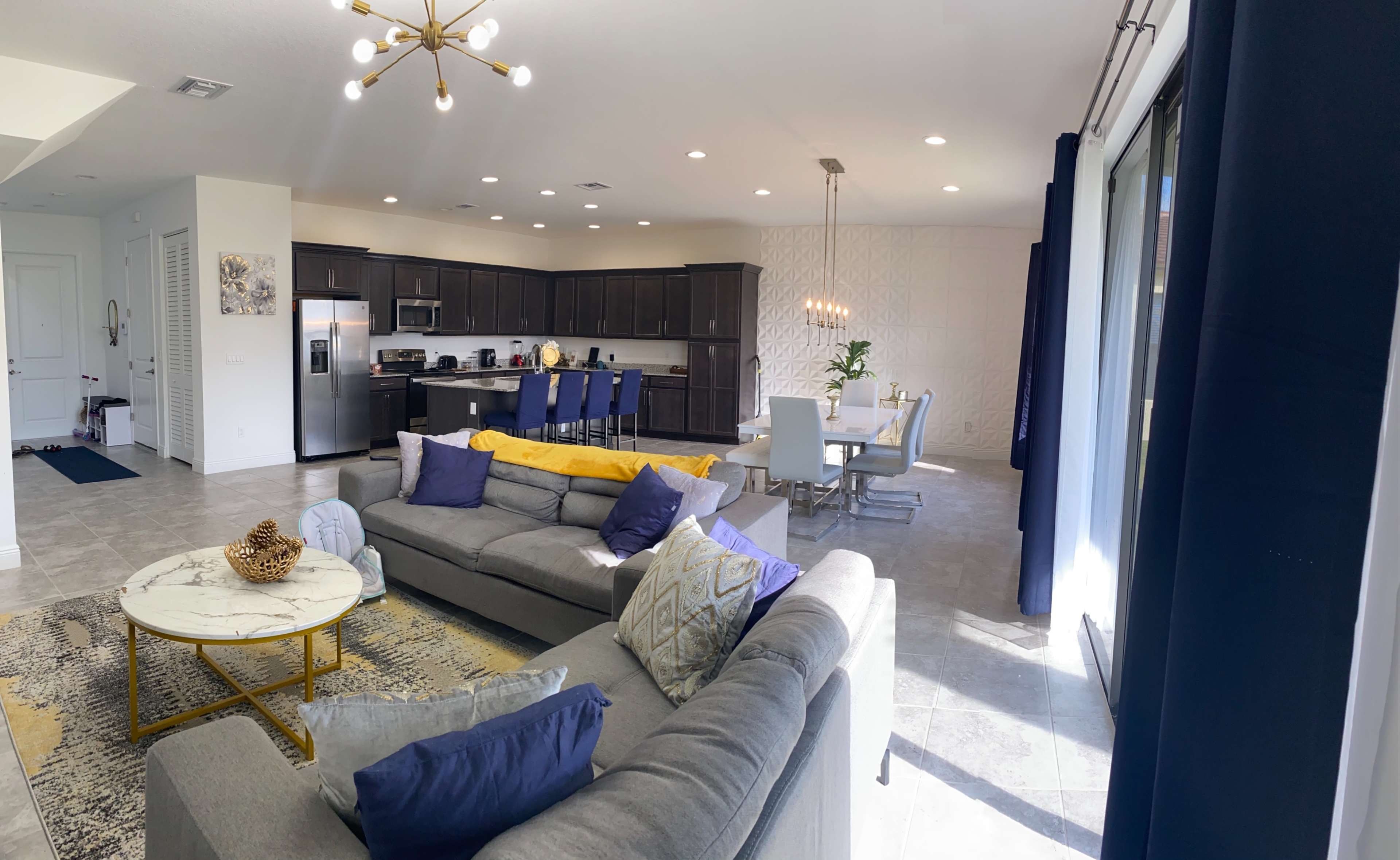 A modern living area with a gray sectional sofa, a marble coffee table, and an adjacent dining space featuring a rectangular table with white chairs.